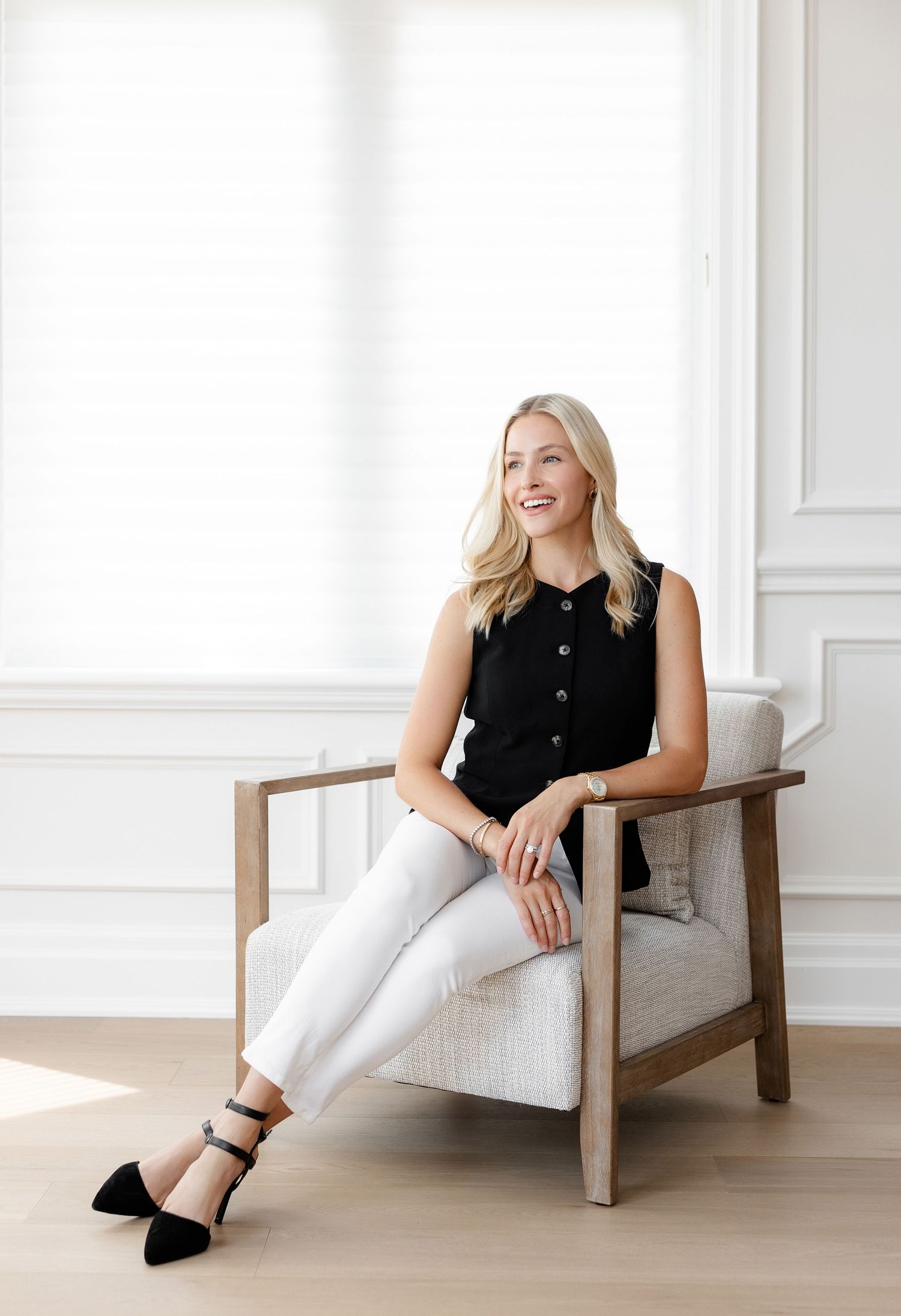 Professional portrait of person in black vest and white pants seated in modern chair.