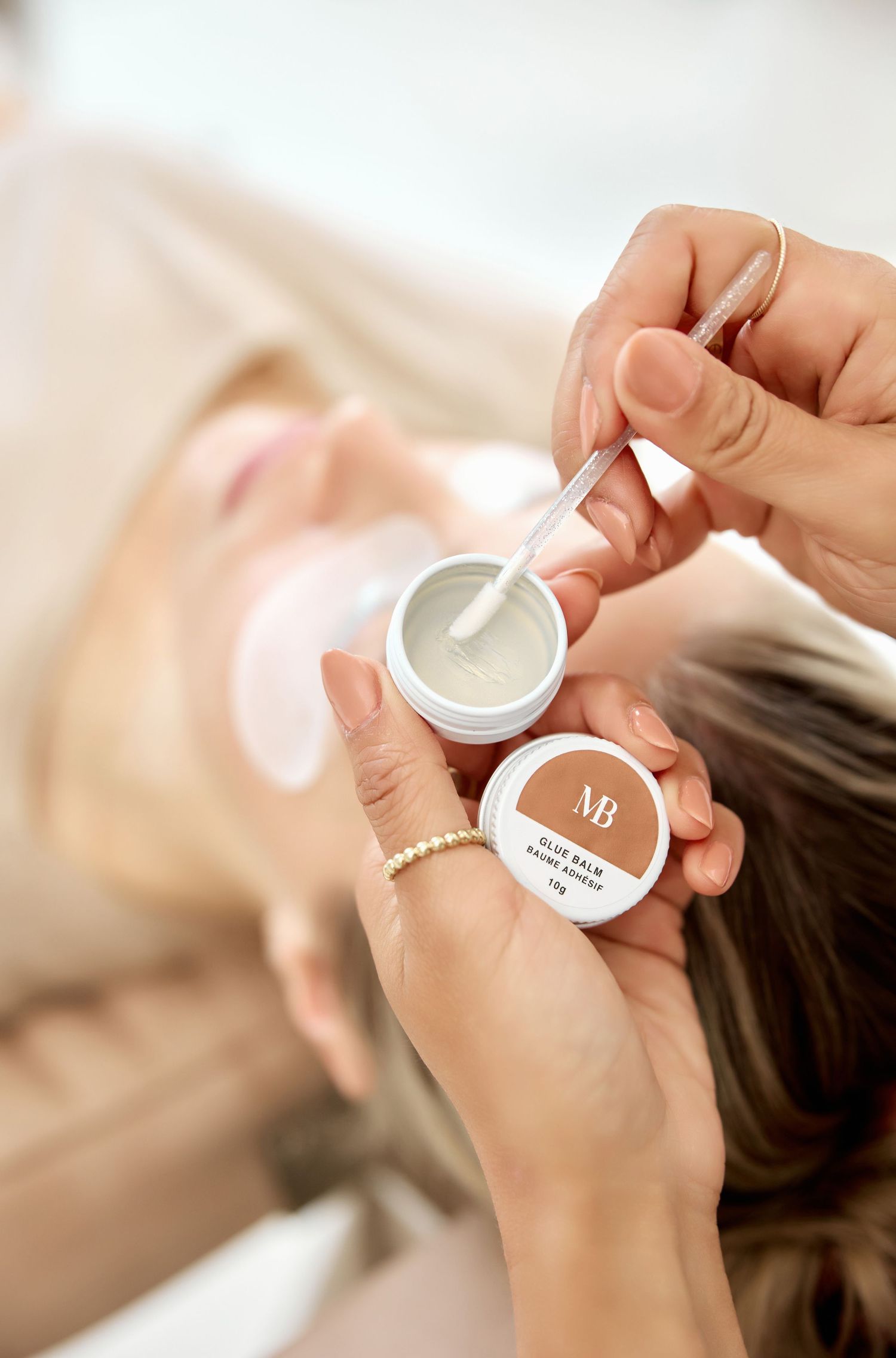 Hands holding and displaying small white beauty product container during treatment.