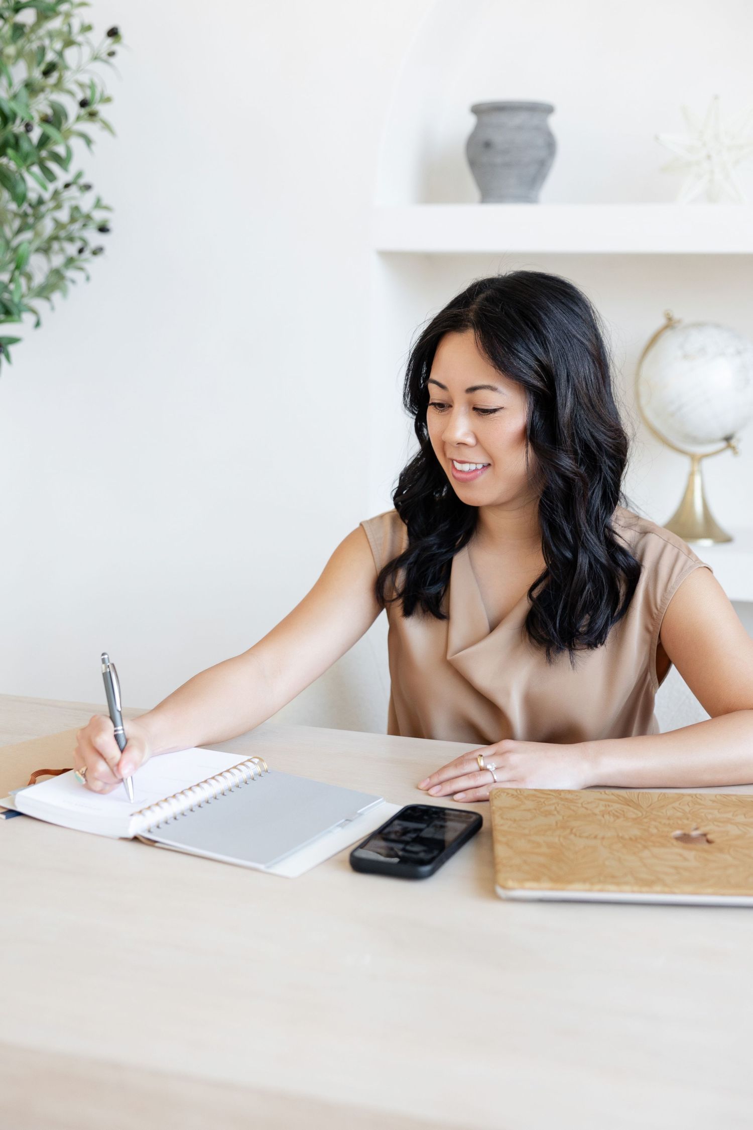 Person writing in notebook at minimalist white desk with decorative elements.
