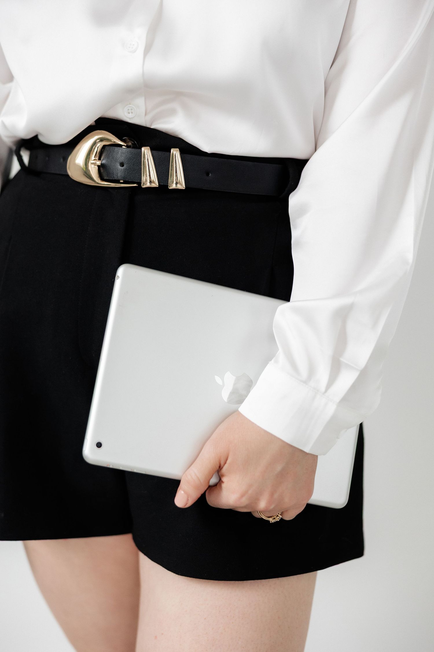 Close-up of black leather belt and white tablet against monochrome outfit.