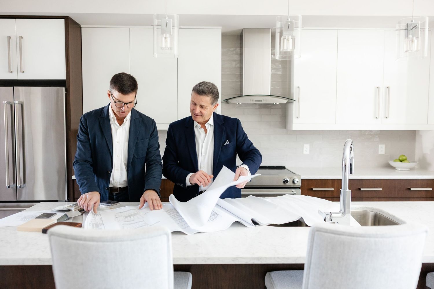 Two professionals reviewing construction plans together in modern white kitchen.