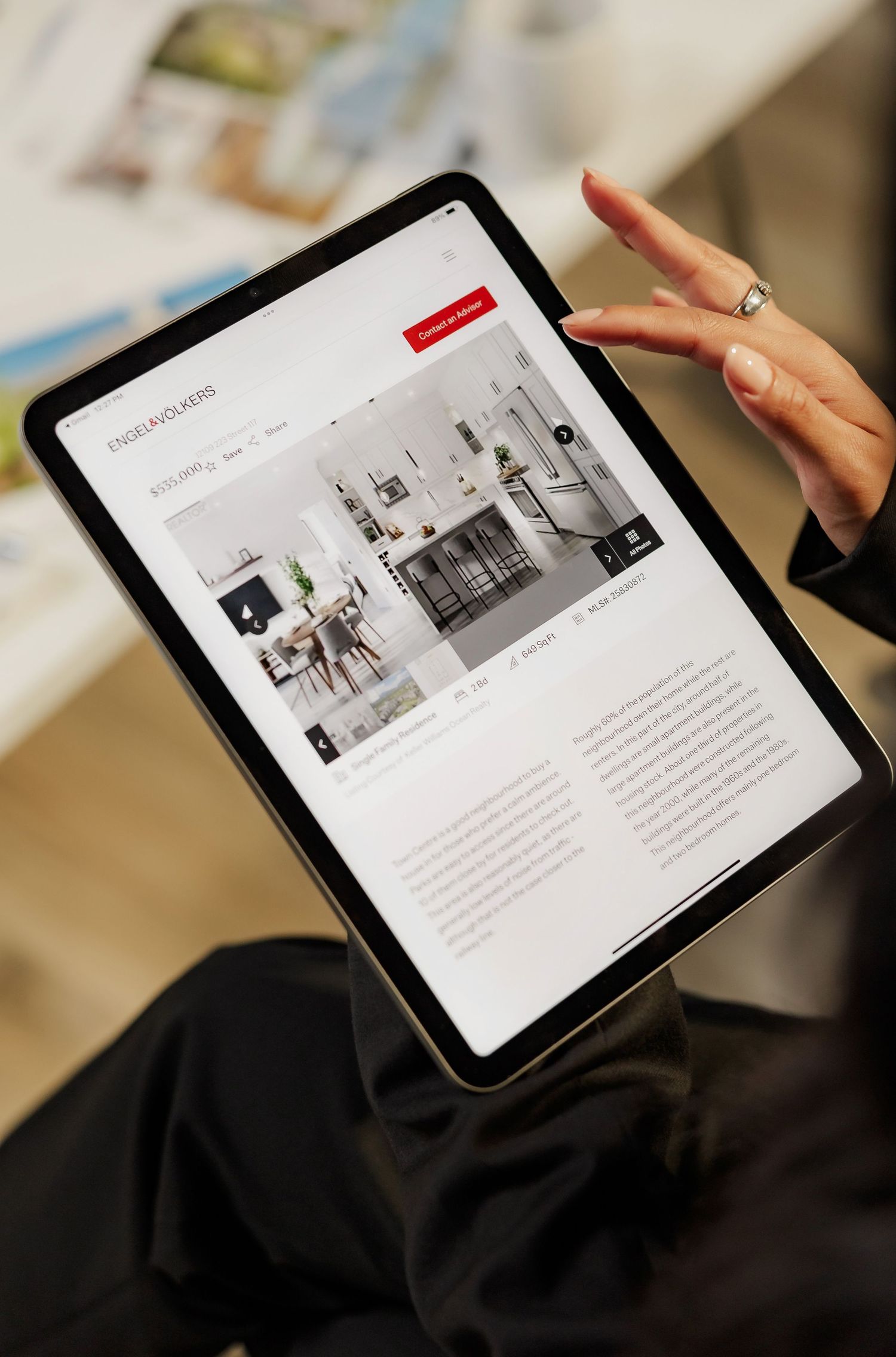 Tablet displaying real estate website with property images and text in modern office setting.
