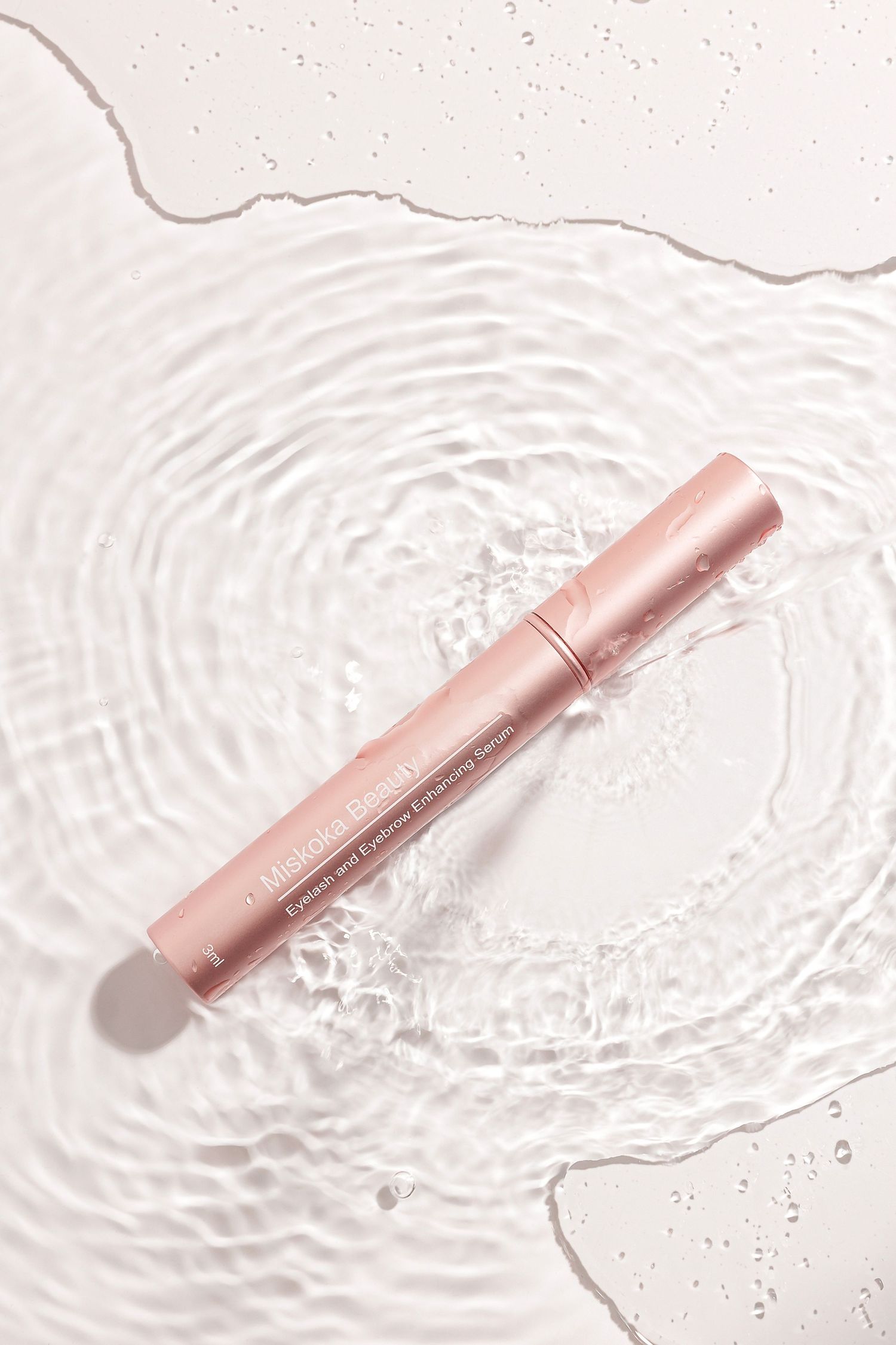 Rose gold cosmetic pen floating on rippling water surface with circular waves.