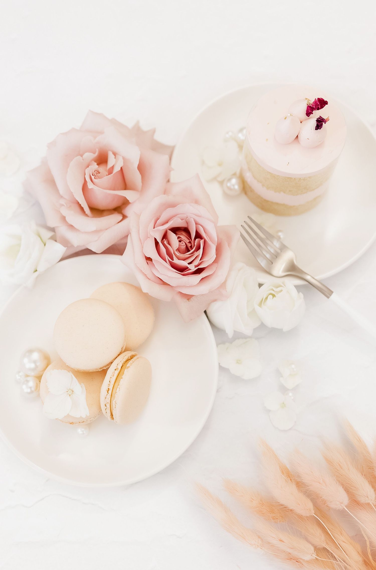 Soft pink roses and macarons arranged on white plates with vintage silverware.