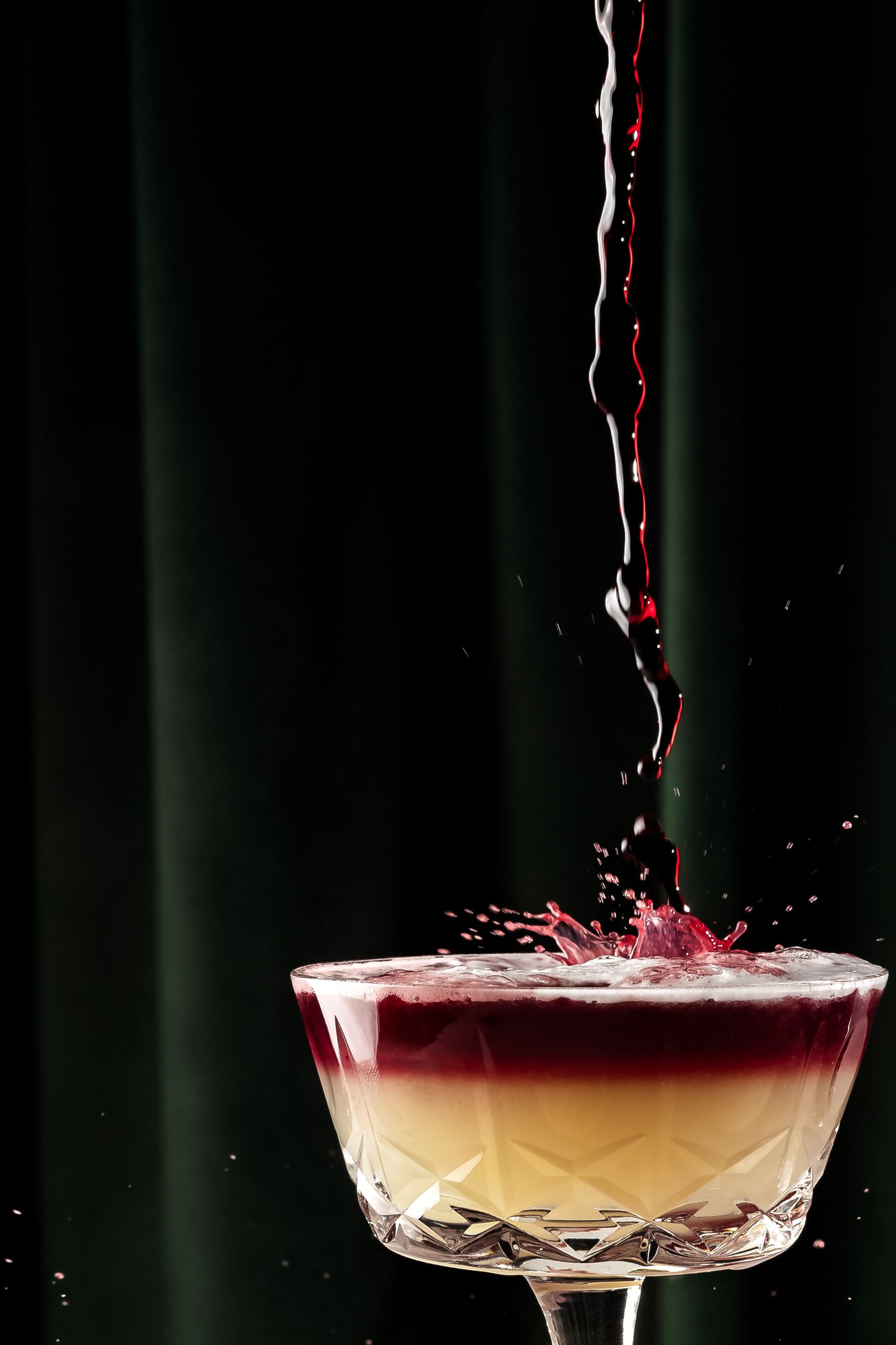 Red liquid splashing dramatically into a coupe glass creating a crown-like effect.