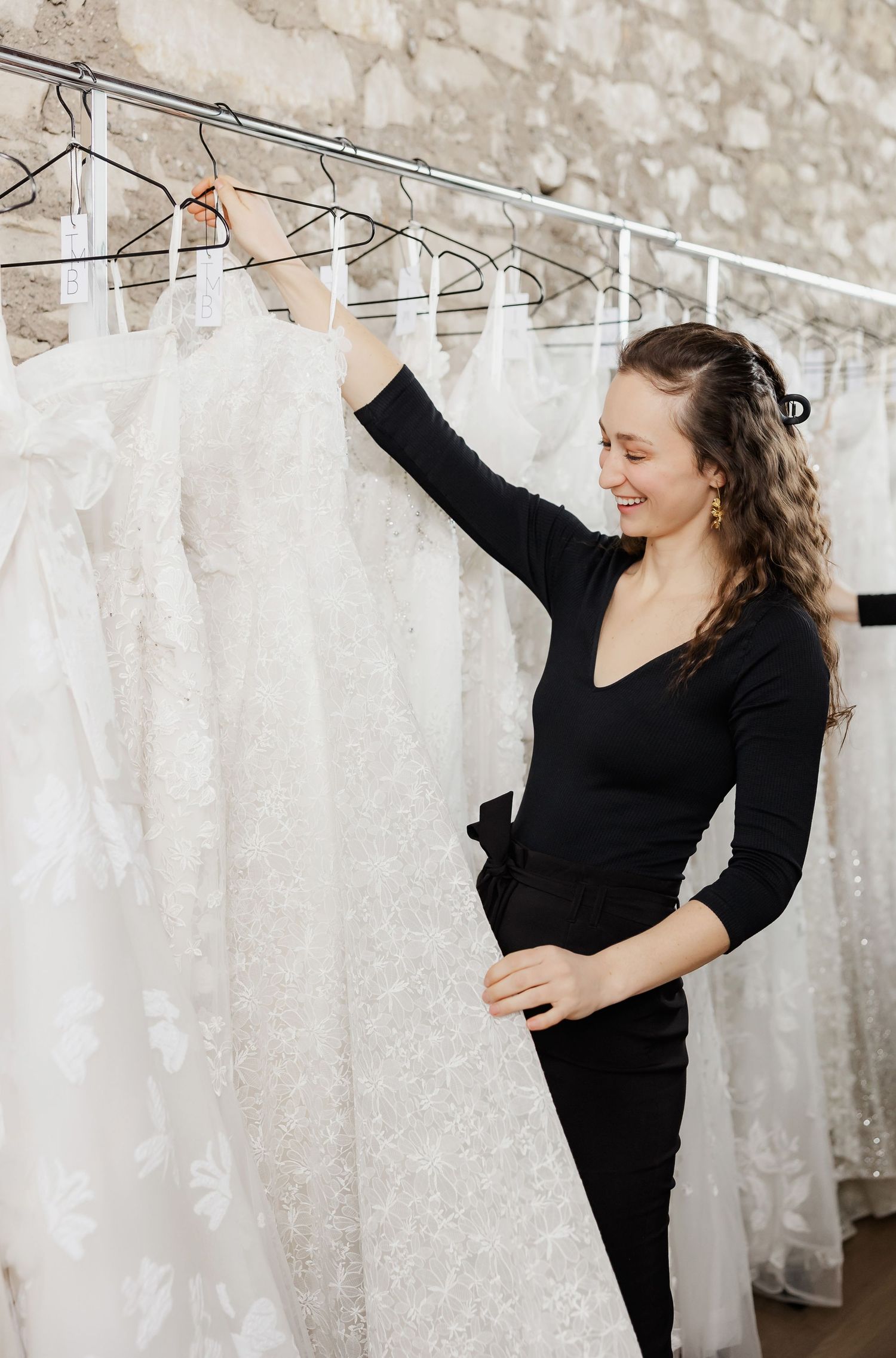 Person in black clothing dancing and posing among white wedding dresses on display.