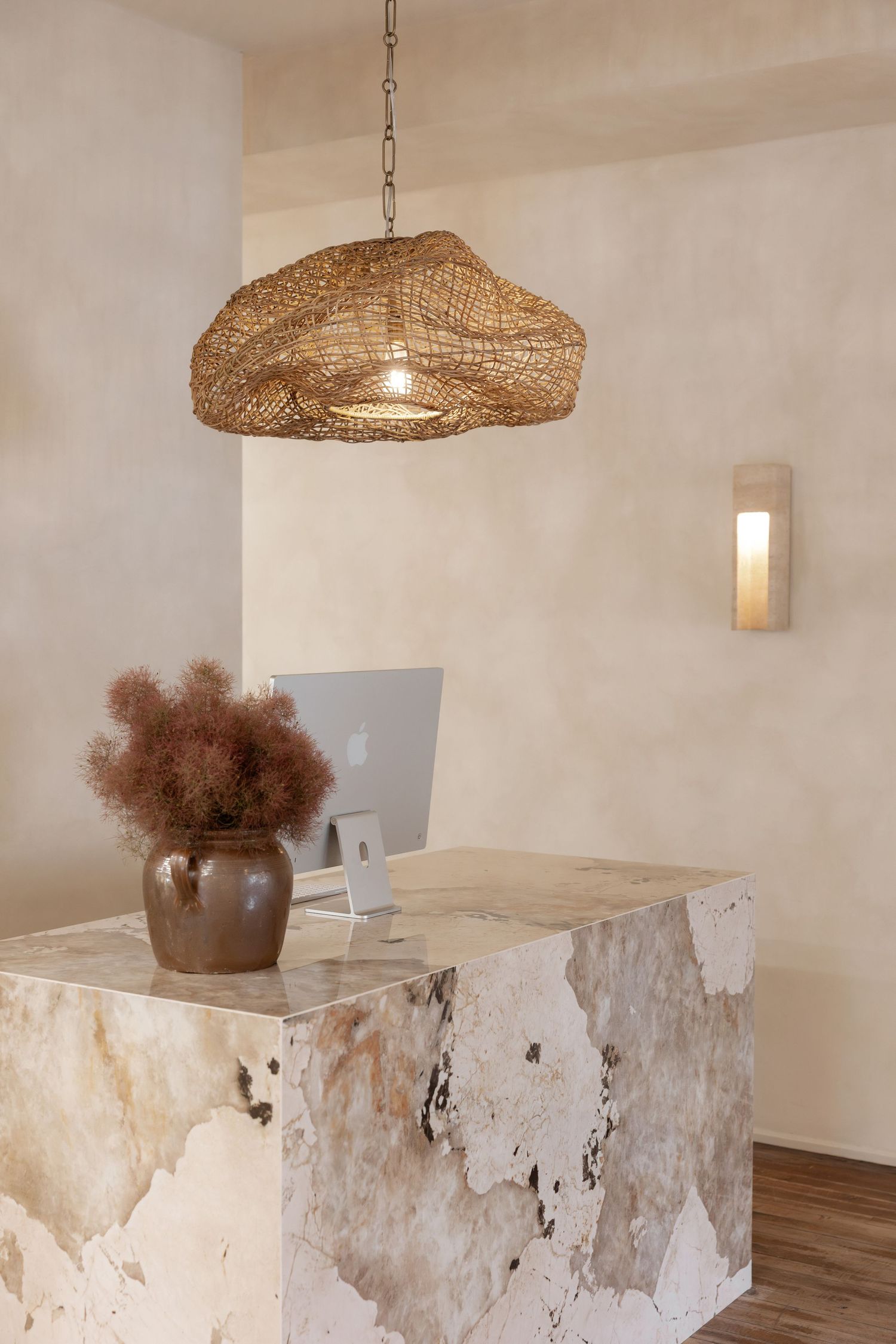 Reception desk made of textured white stone with woven pendant light and natural decor.