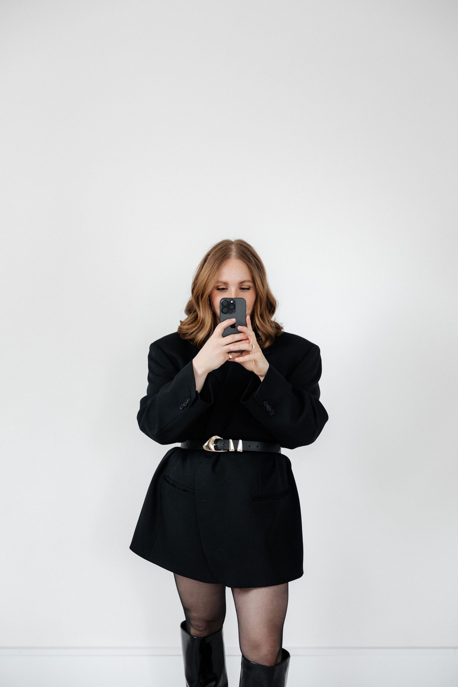 Stylish figure in black ensemble creates dramatic poses while holding mobile device.