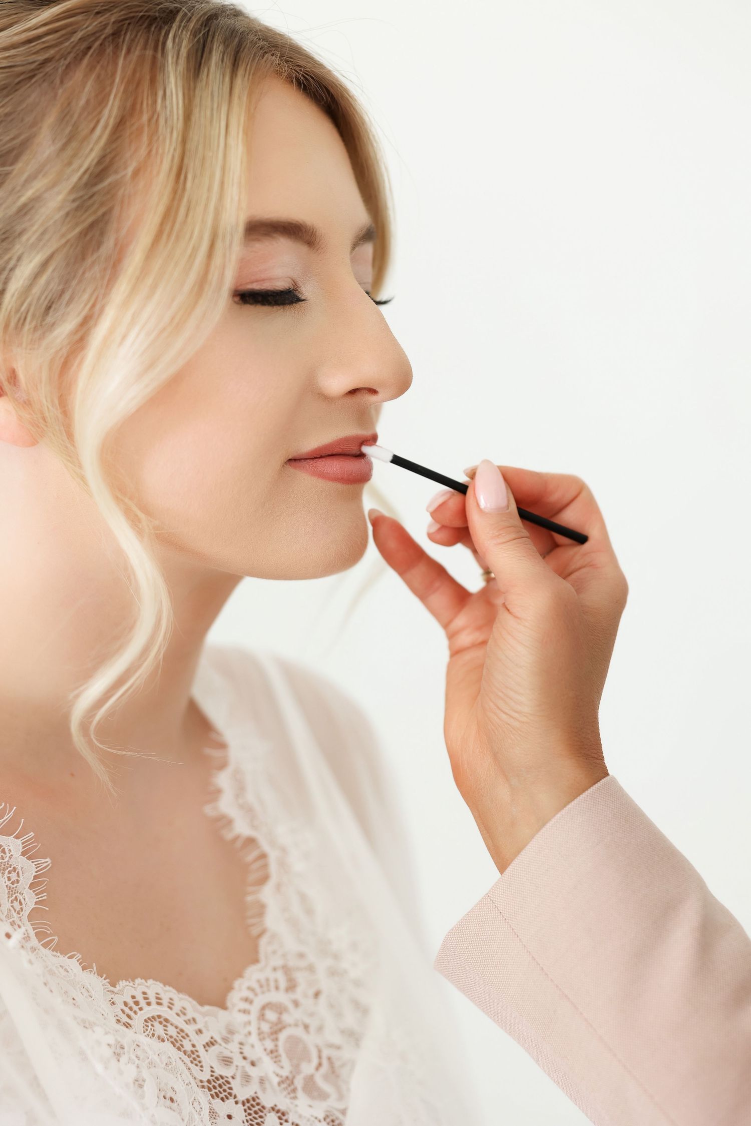 Makeup artist applying lip color in elegant white lace setting.