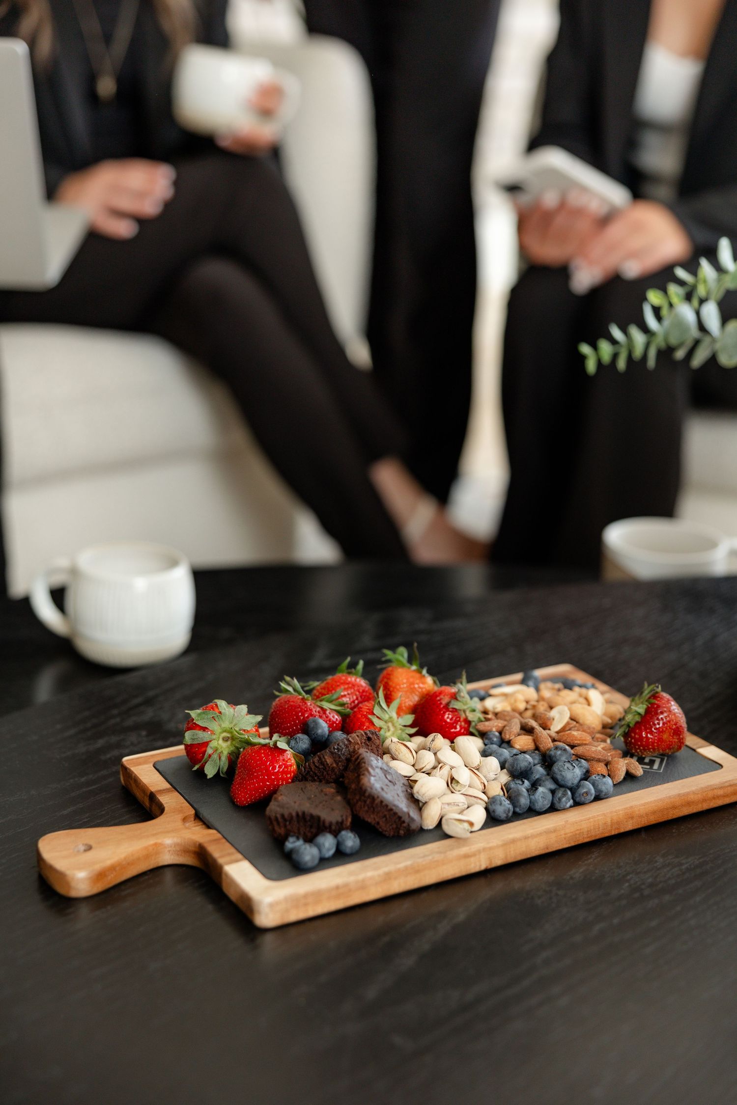 Wooden charcuterie board with fresh berries, nuts and snacks on dark surface.