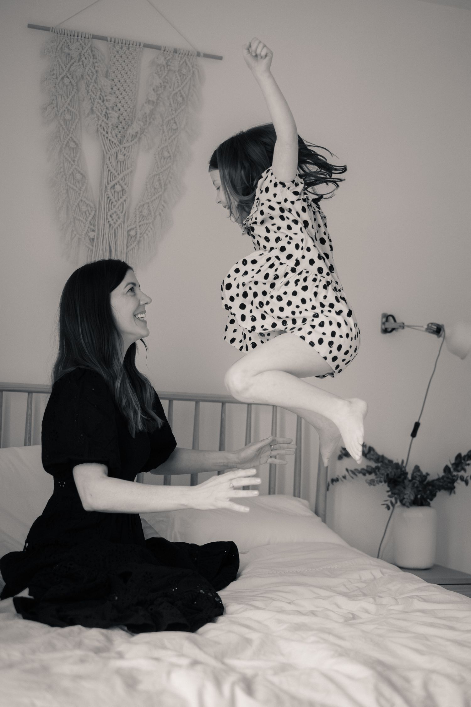 Girl jumping on a bed with her mother, who is smiling at her. Having fun at home on a photo session. With Lucy Chaplin