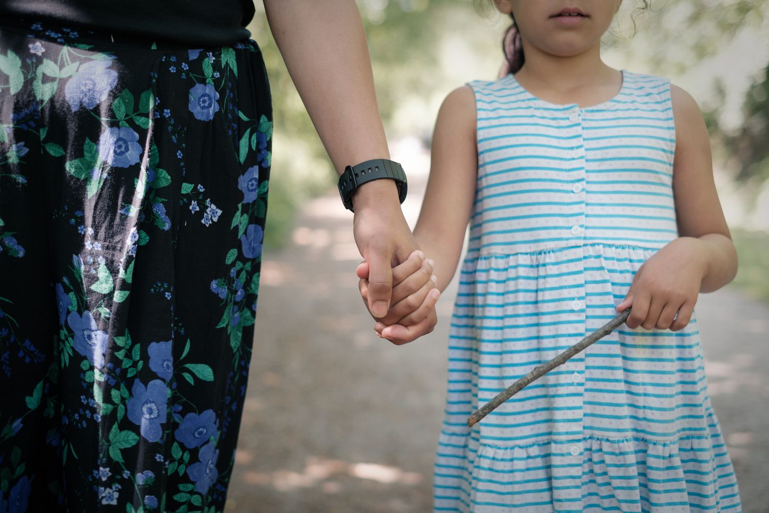 Mother and daughter holding hands during an outdoor shoot. Girl holding a stick, in natural dappled light in Slaithwaite, Huddersfield.