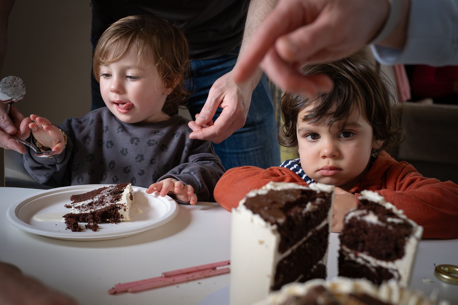 Young children at looking at a big cake at home during a birthday party. Candid and natural photography, Lucy Chaplin family photographer.