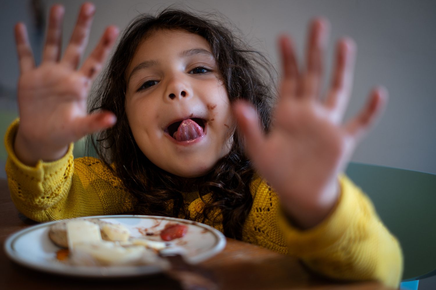 Girl holding hands up with chocolate on hands, candid and genuine moment at the table while eating. Looking at Lucy for the photograph.