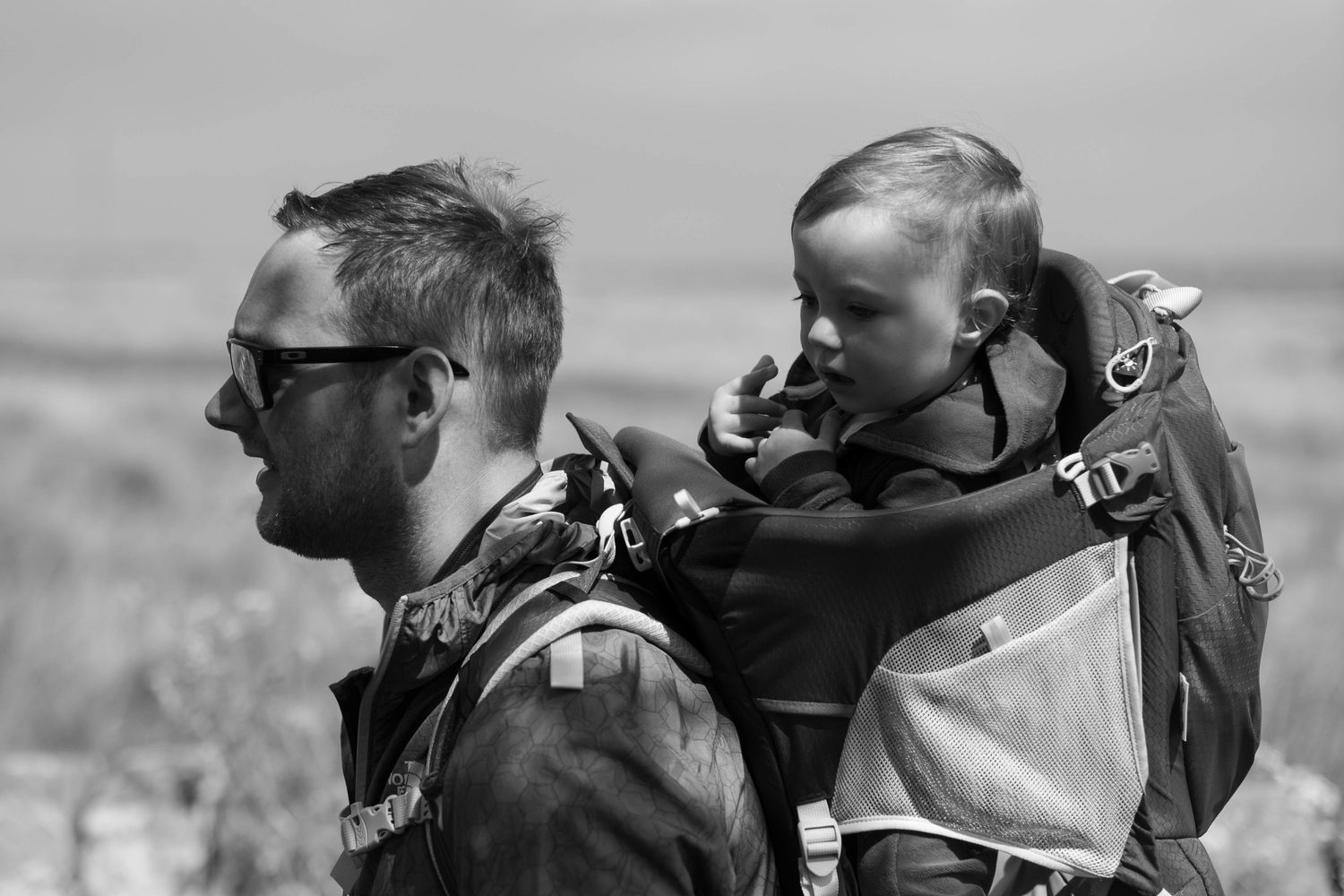 Father carrying baby in carrier on a walk in the sun in natural light. On the Huddersfield moor, by Lucy Chaplin. West Yorkshire.