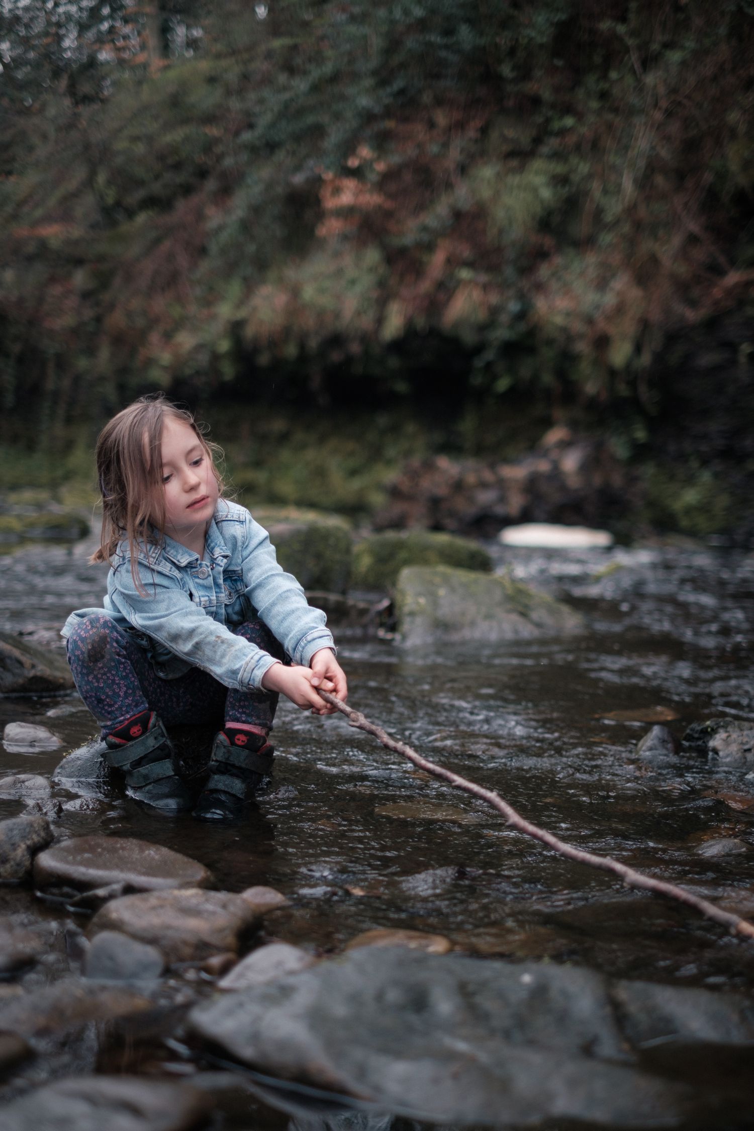 Girl holding a stick playing in a river in natural light,  outside during a shoot with Lucy Chaplin, Slaithwaite, Huddersfield, Yorkshire