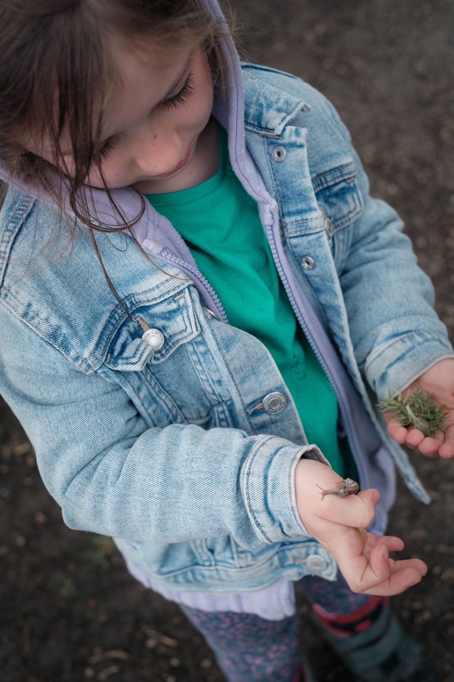 Girl holding a snail near a river in natural light, playing outside during shoot with Lucy Chaplin, Slaithwaite, Huddersfield, Yorkshire