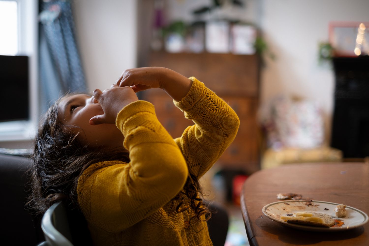Girl is eating at the table at home during a family photo session. Natural, unposed photo. By Lucy Chaplin.