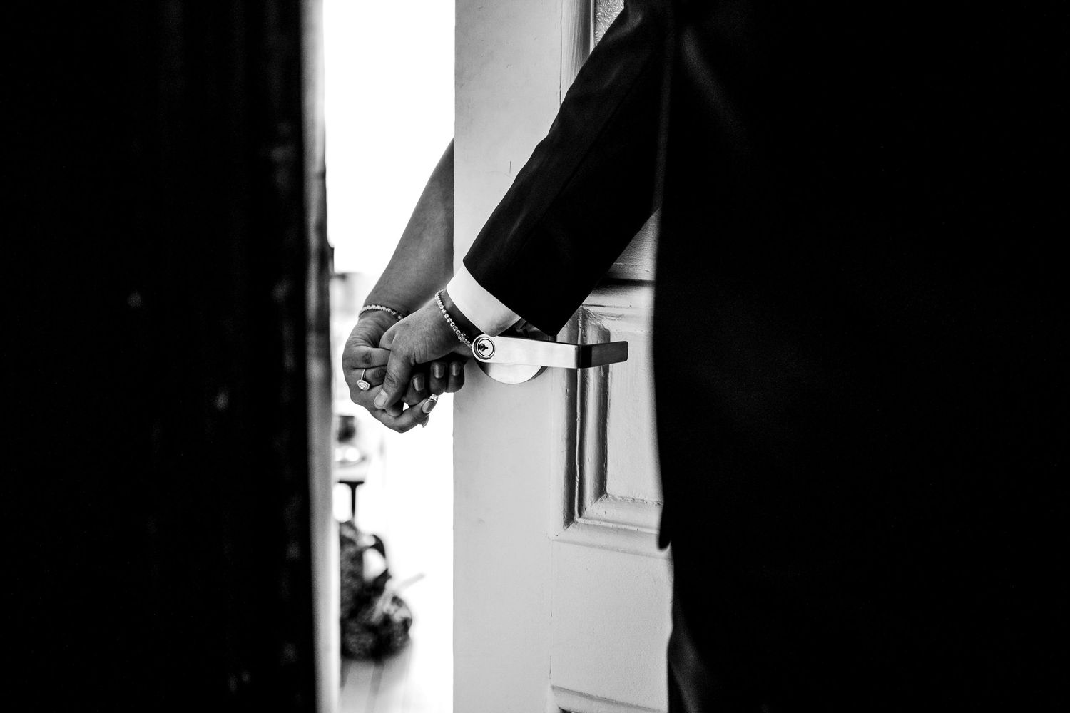 Black and white wedding detail photo of a groom's hand reaching for a door, captured in an intimate, editorial style.