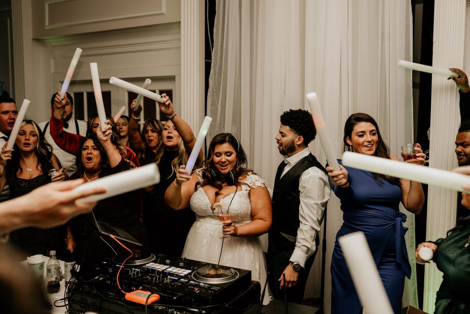 Wedding guests dance and celebrate on a crowded dance floor with raised hands and joyful expressions.