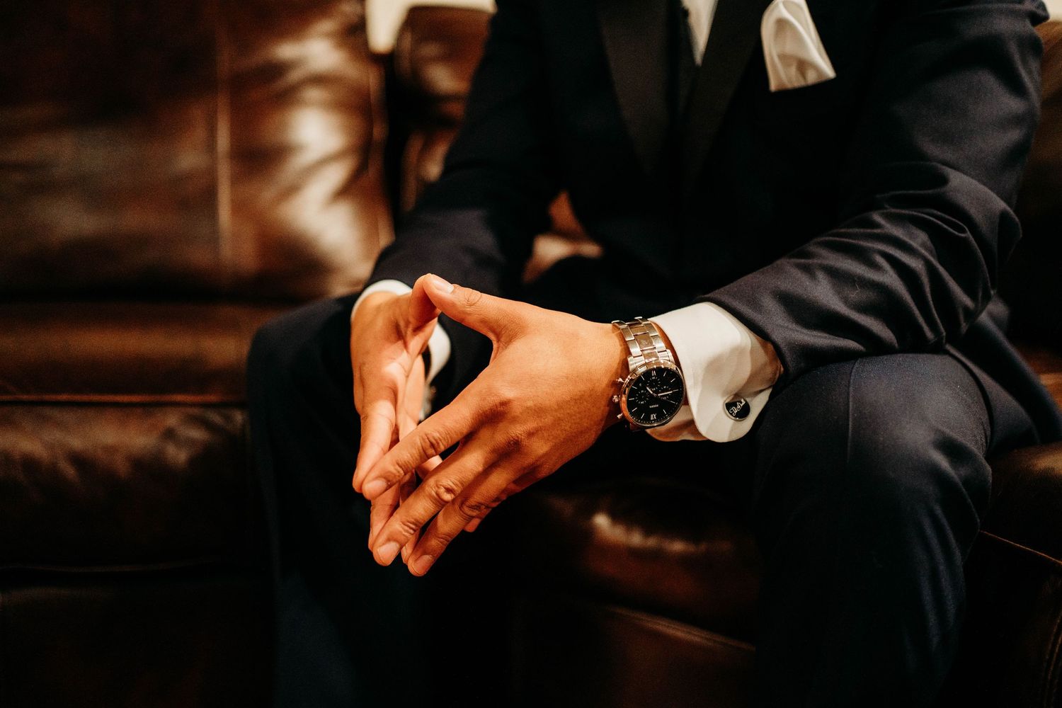 Close-up shot of the groom's hands adjusting cufflinks on a formal black suit sleeve.
