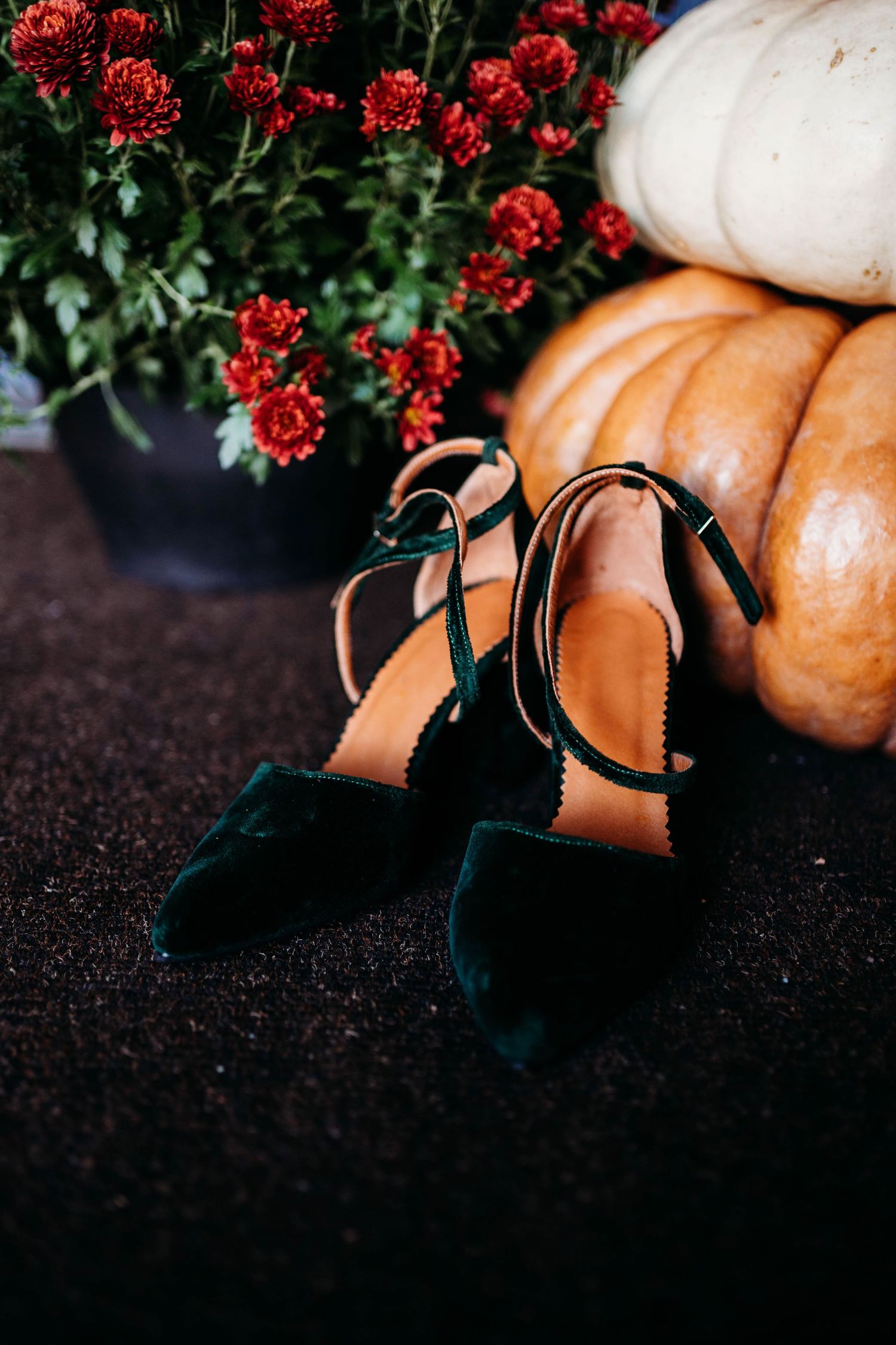 Wedding detail photo of green velvet heels styled with red florals and textured elements in a moody arrangement.