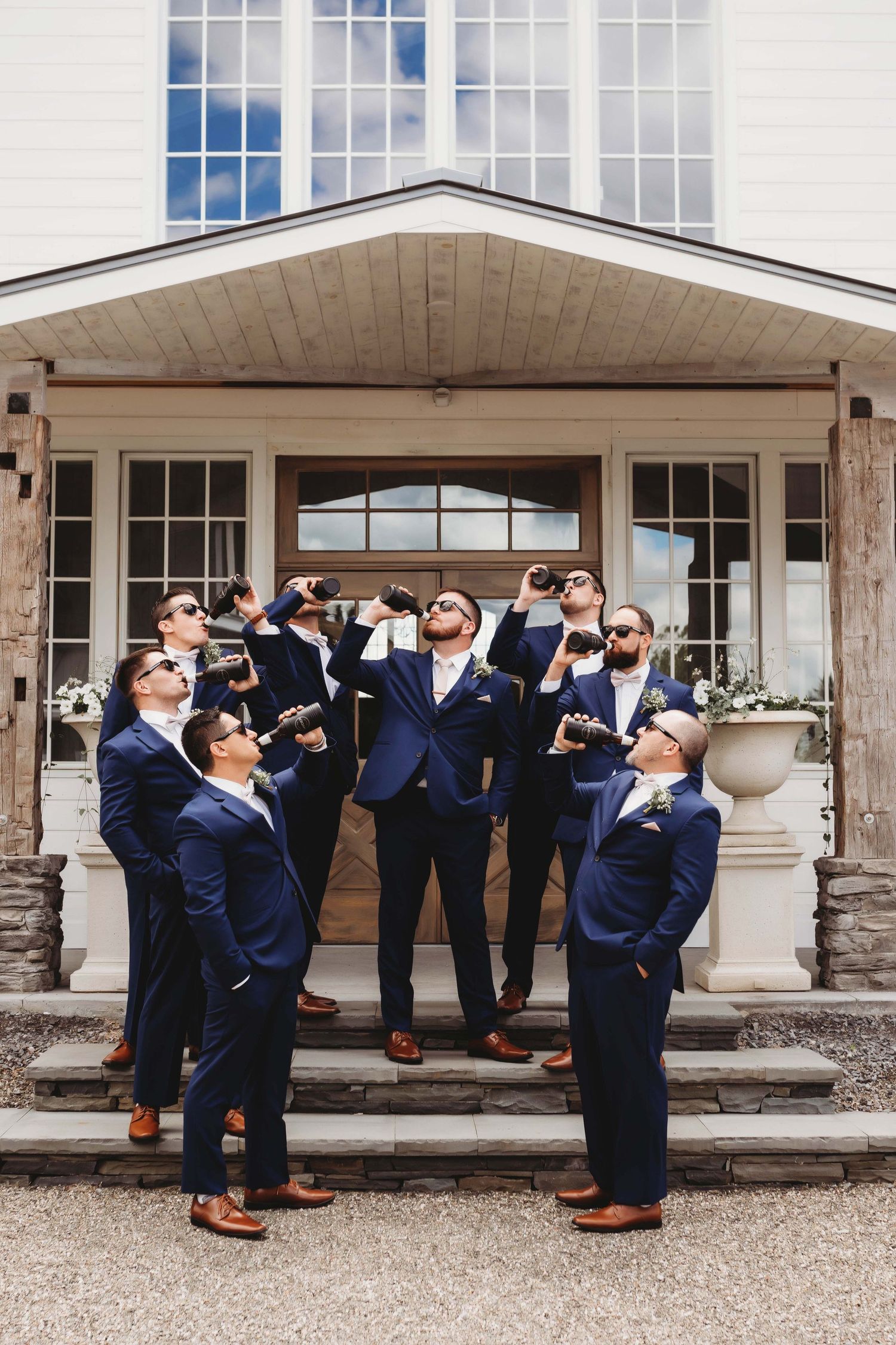Groomsmen in matching navy suits strike a playful pose on mansion steps while looking up at the sky.