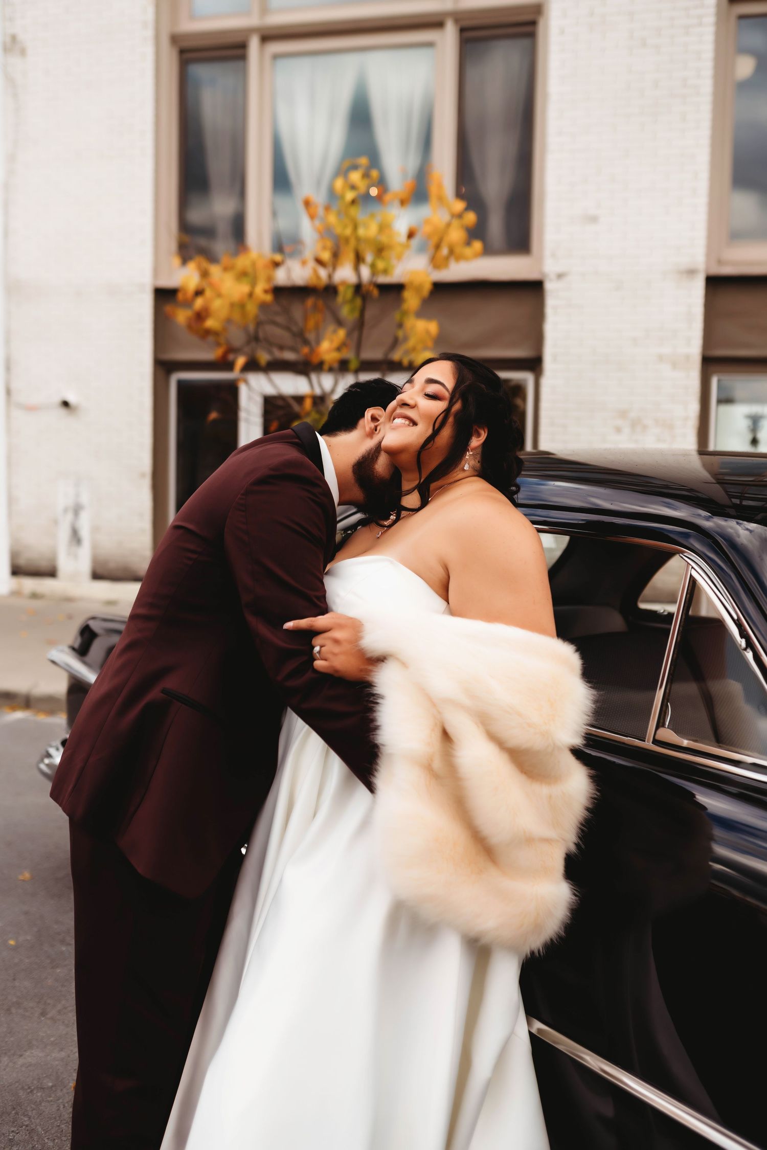 Couple shares an intimate moment outdoors, with the bride wearing a white dress and a cream fur wrap.