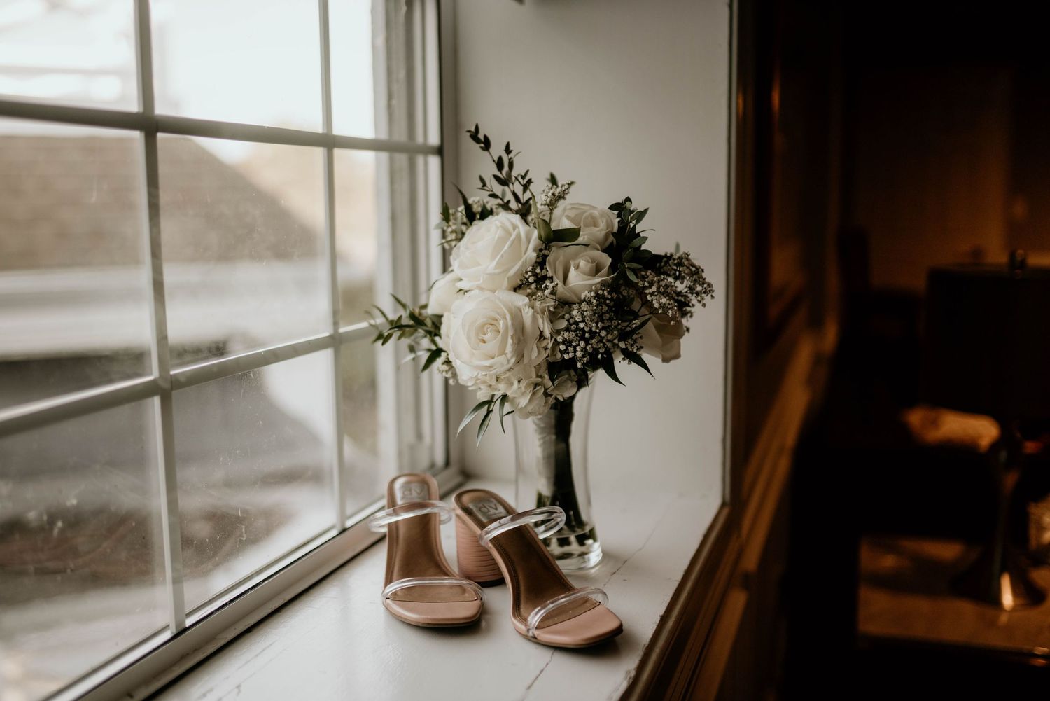 Elegant windowsill with delicate floral arrangement and natural light streaming in. Bridal detail shot