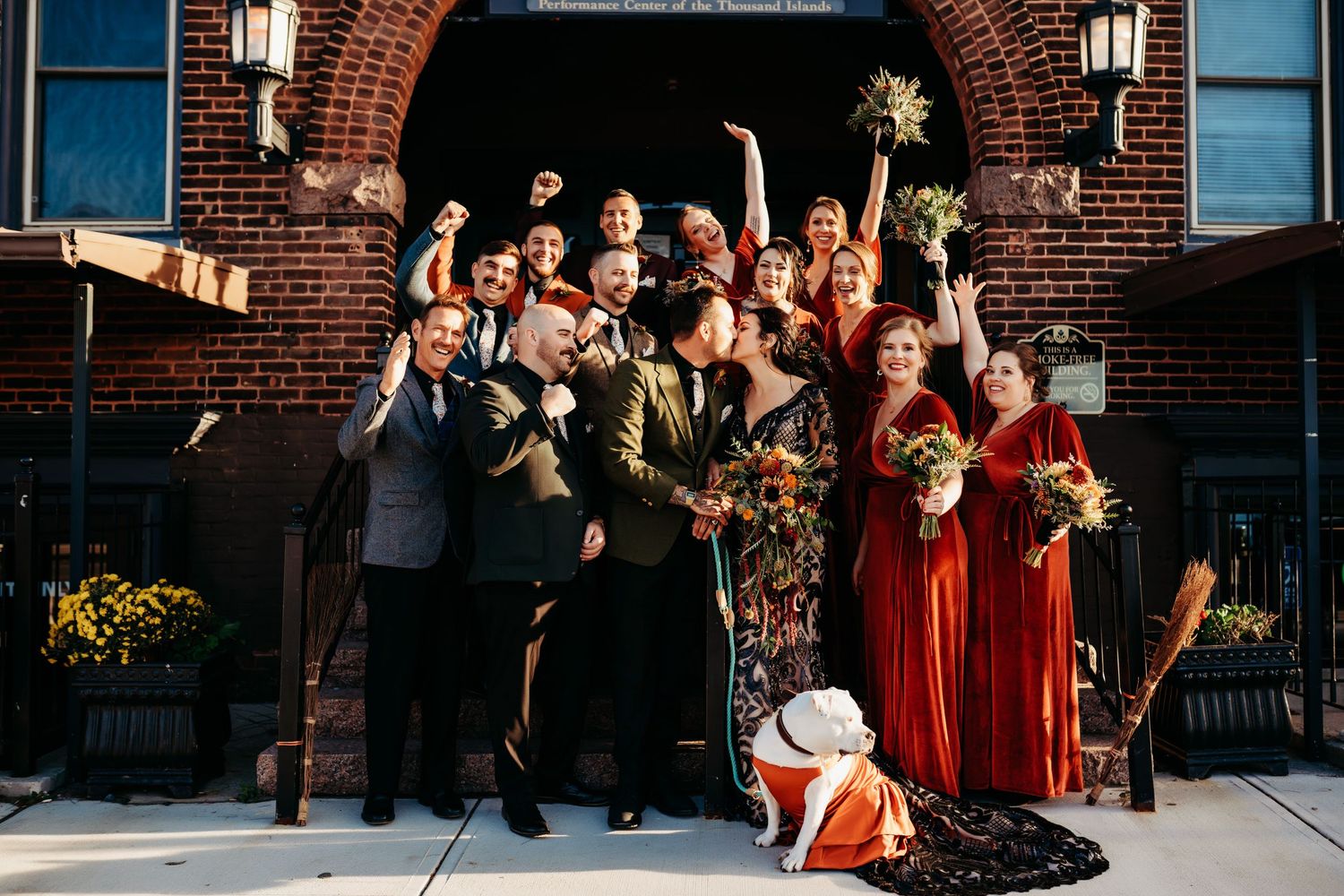 Wedding party celebrating together outside a brick building, with bridesmaids in deep red dresses.