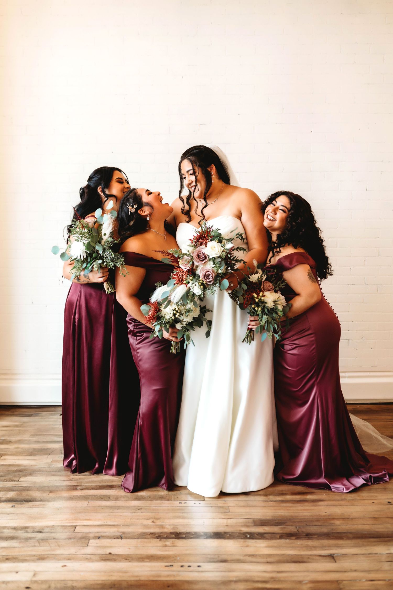 Bridal party in burgundy dresses posing together with bouquets, captured in a candid wedding photography style.