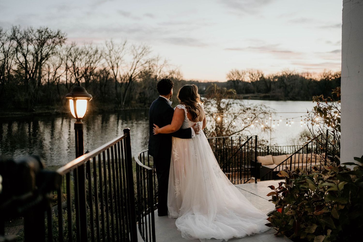 Bride and groom share a romantic sunset wedding scene overlooking a lake with silhouettes against the golden sky.