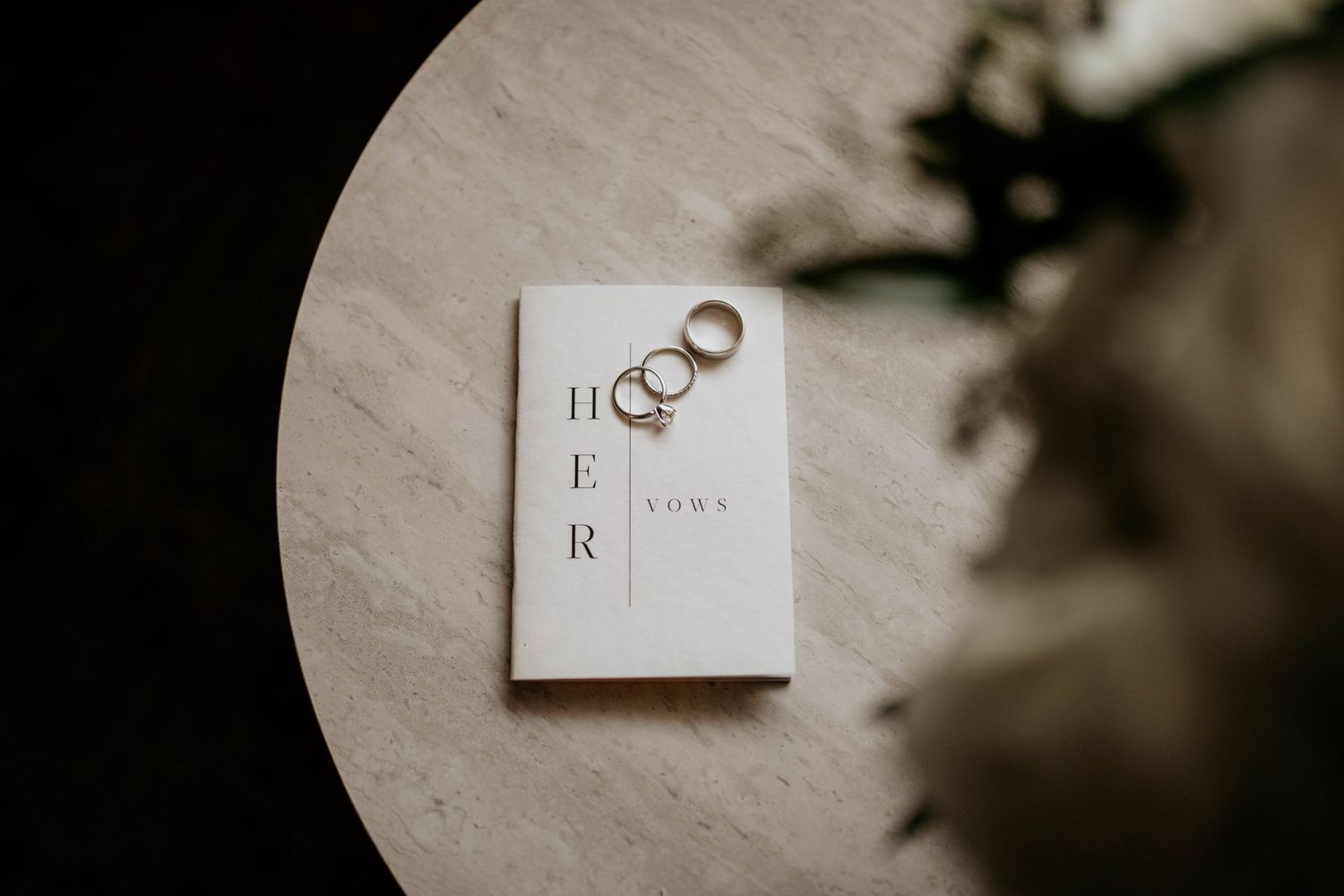 Minimalist wedding stationery and rings styled on light surface with soft shadows.