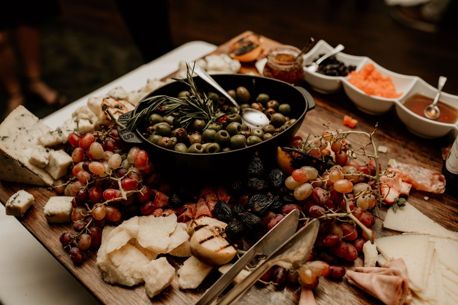 A rustic charcuterie board with meats, cheeses, olives, and various dipping sauces arranged on a wooden surface.
