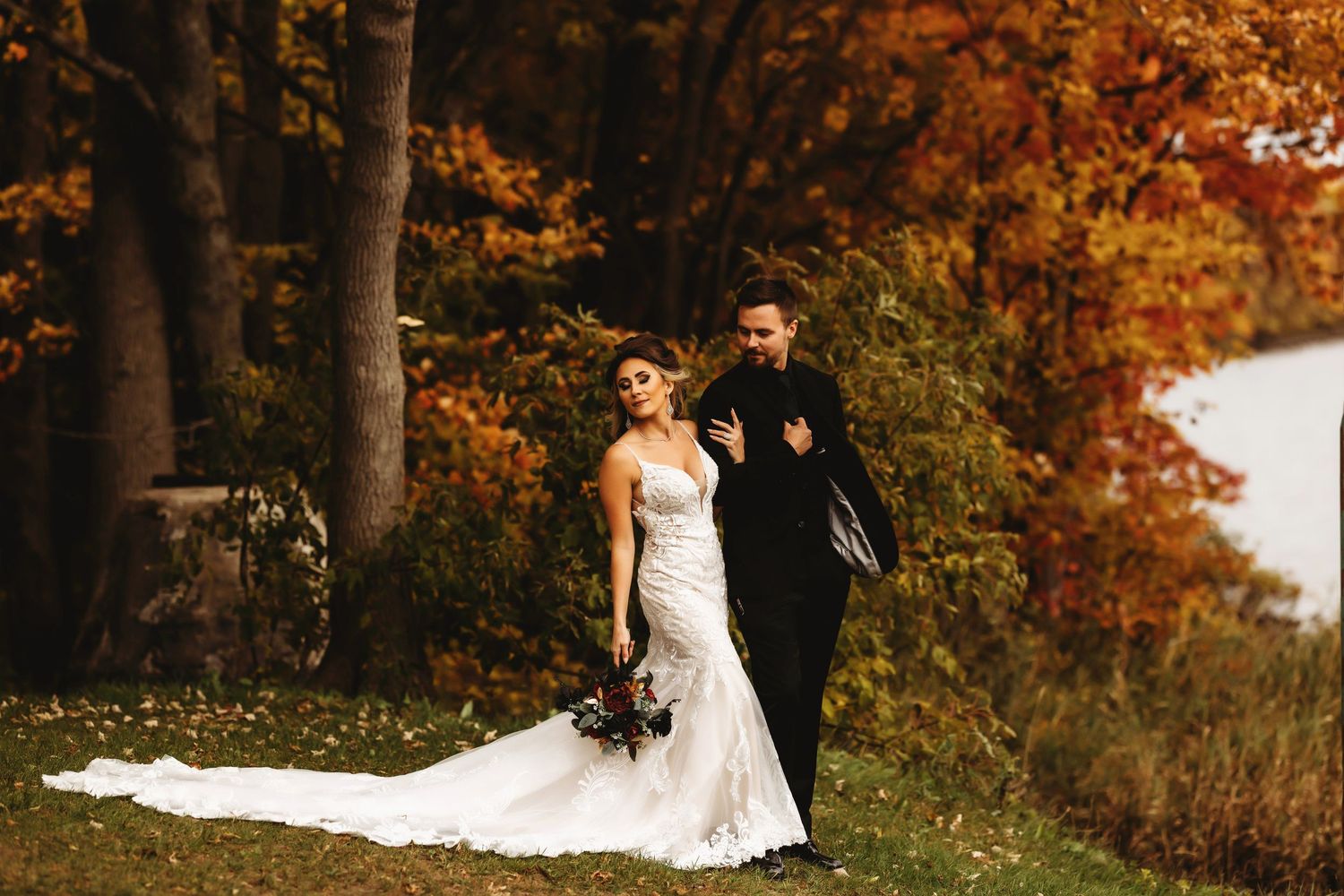 A wedding couple shares an intimate moment in a vibrant autumn forest setting with golden leaves surrounding them.