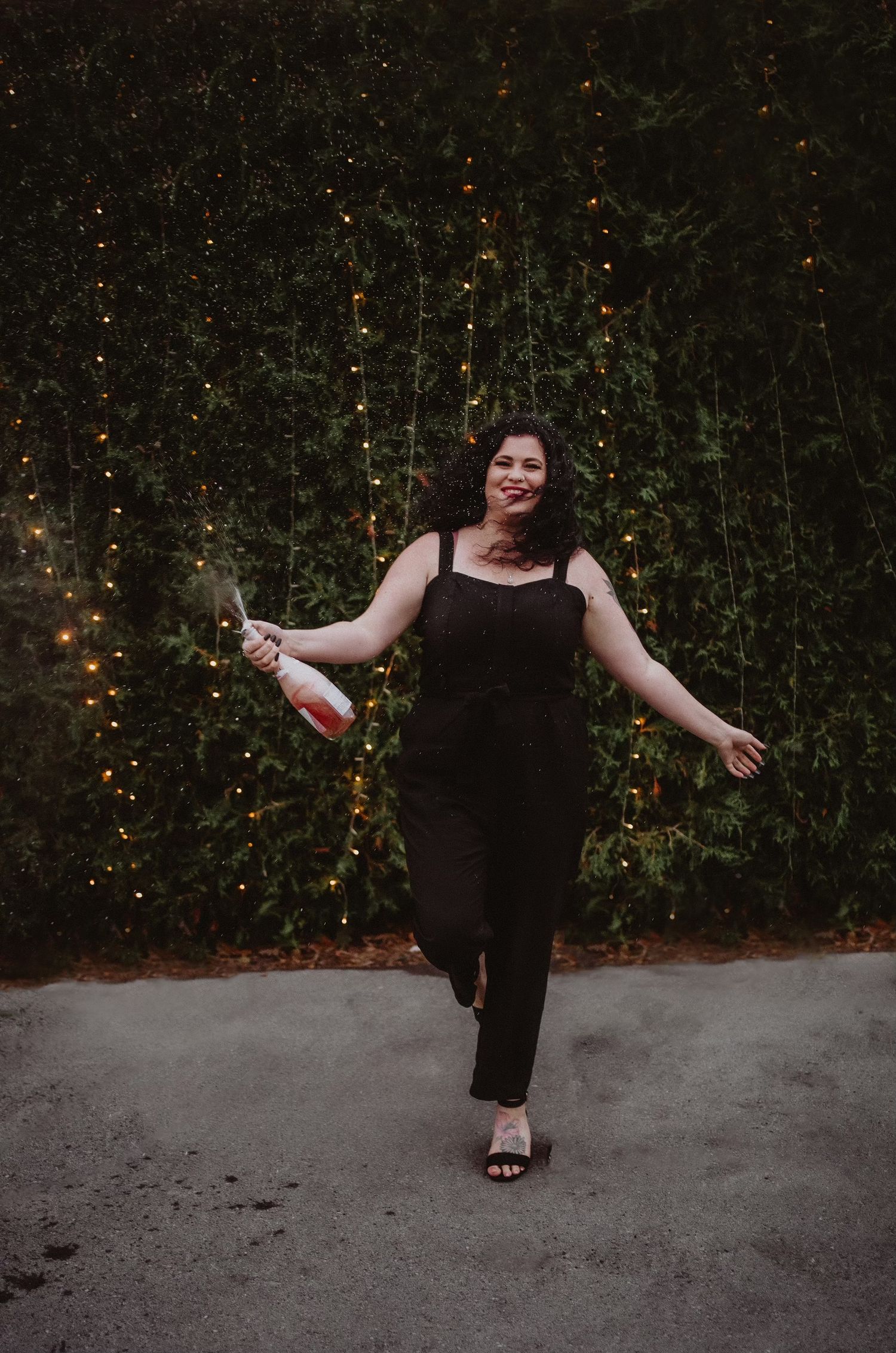 A person in black clothing strikes dynamic dance poses against a backdrop of twinkling lights and greenery.