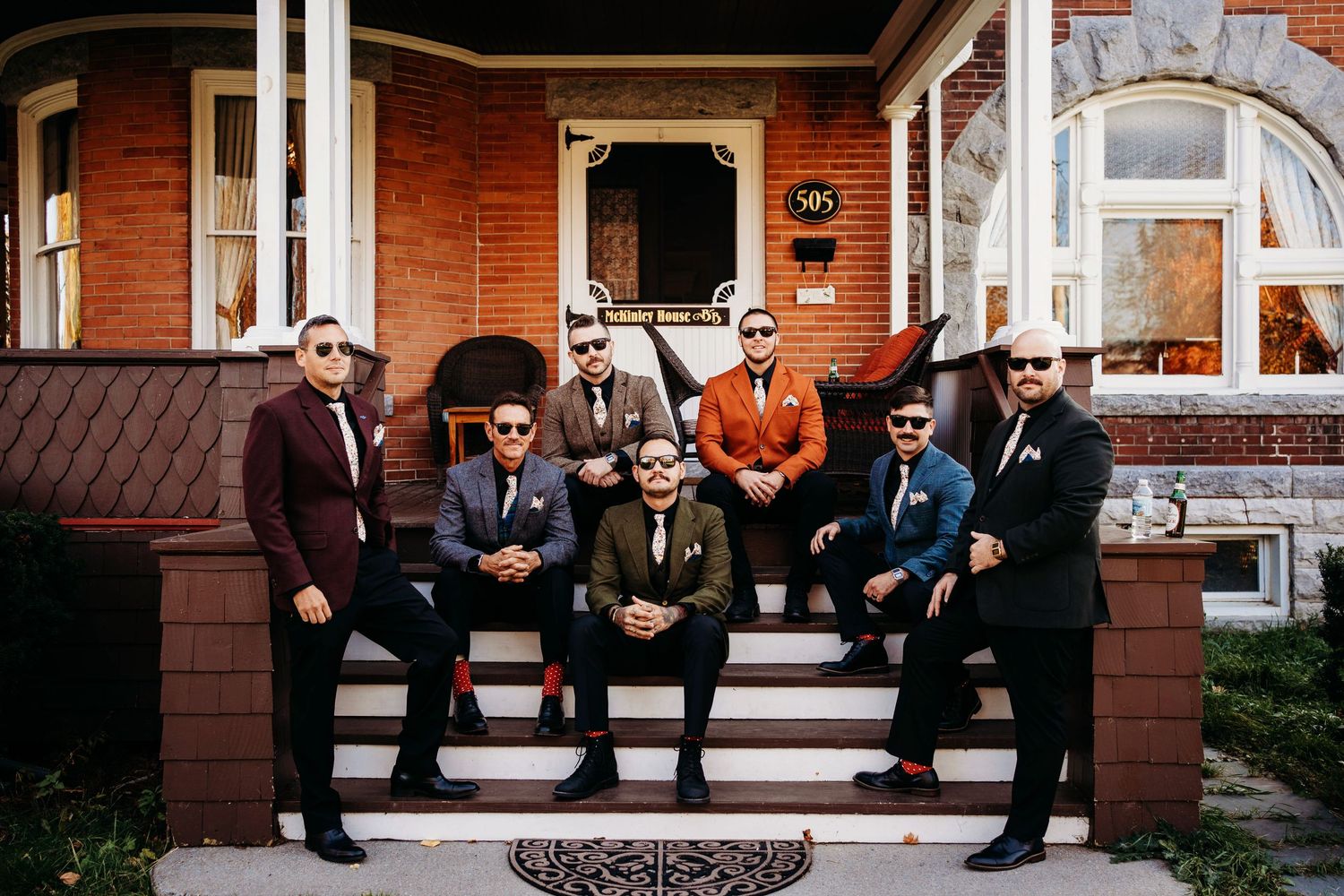 Groom and groomsmen posing together in coordinated suits on outdoor steps during a wedding day.
