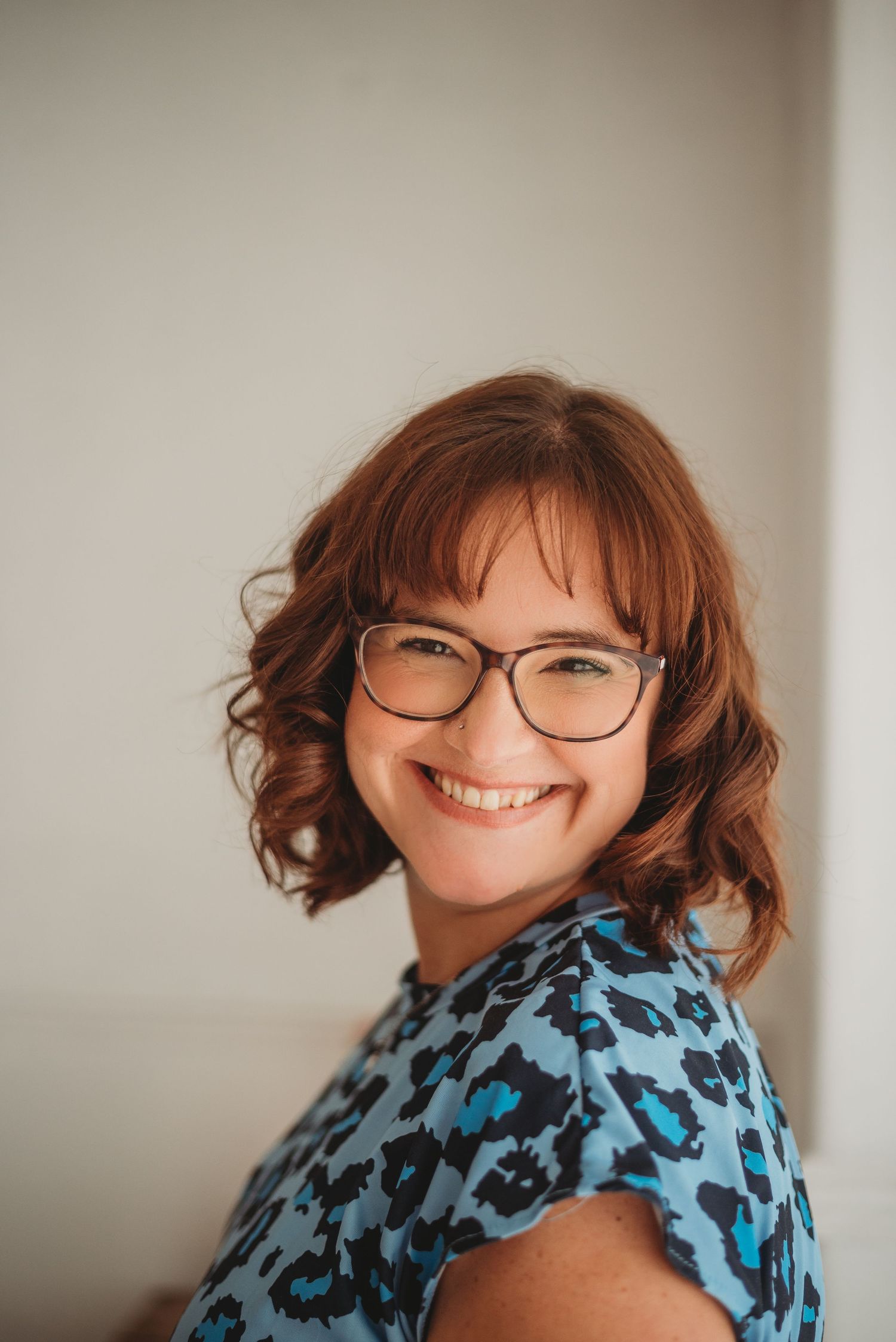 Smiling female marketing consultant wearing glasses, photographed indoors against a neutral background.