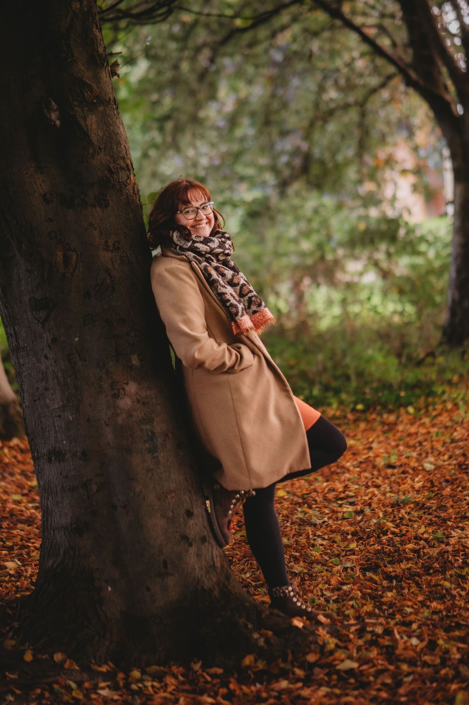 Creative marketing consultant standing outdoors among autumn leaves, smiling and wearing glasses, a scarf and a coat.