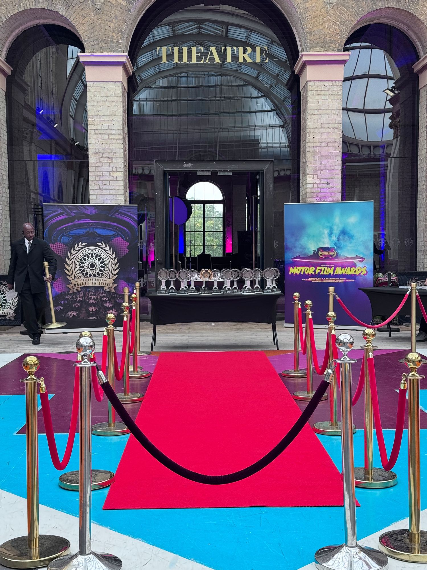 Red carpet entrance with velvet ropes and Theatre sign illuminated in elegant archways with blue accent lighting.