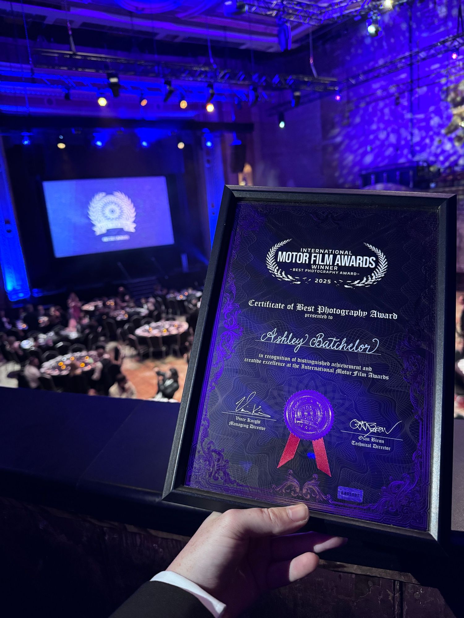 Awards ceremony venue illuminated in blue lighting with digital screens displaying certificates and achievement badges.