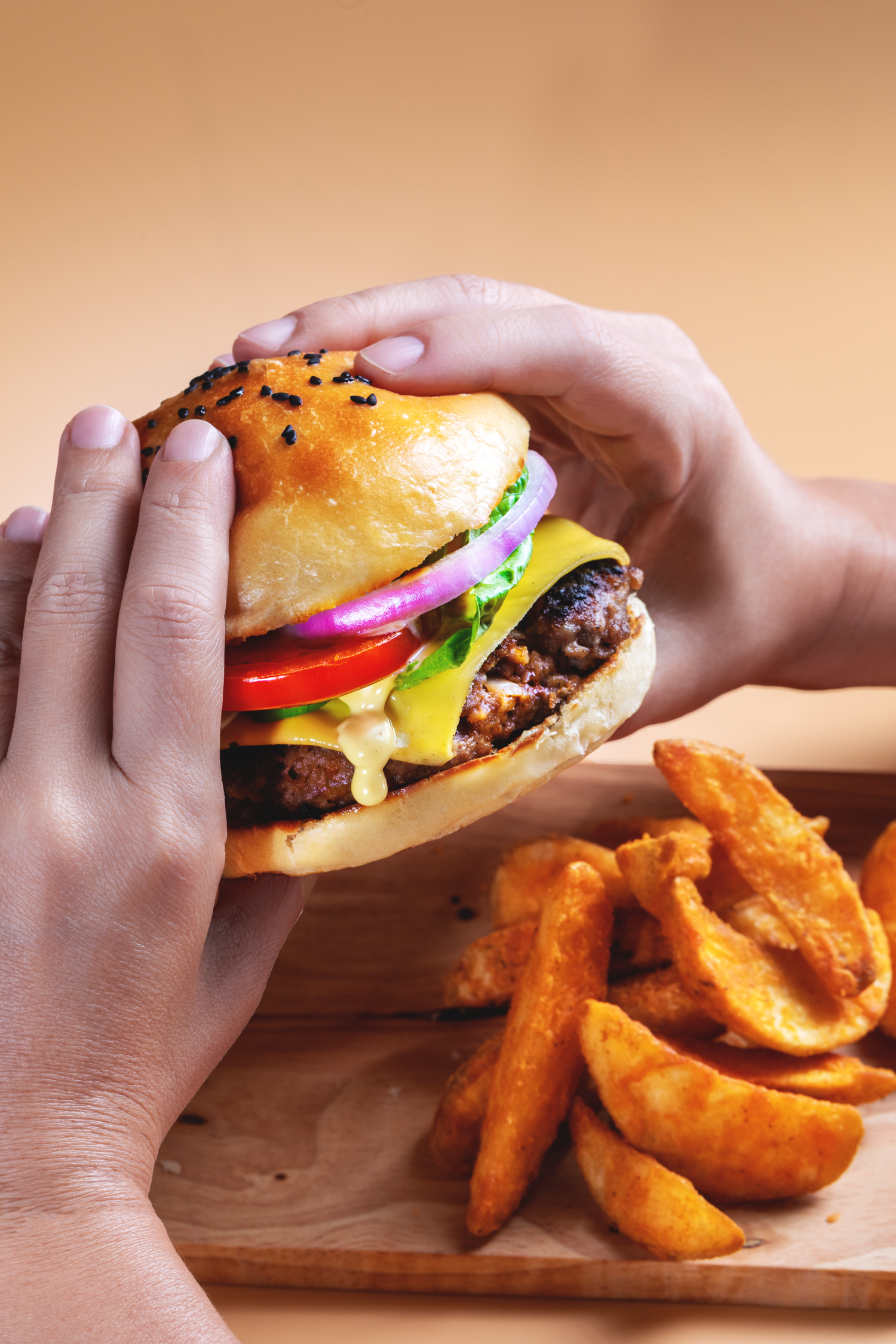 Commercial food photography featuring a gourmet burger held by hand with potato wedges and fresh ingredients.