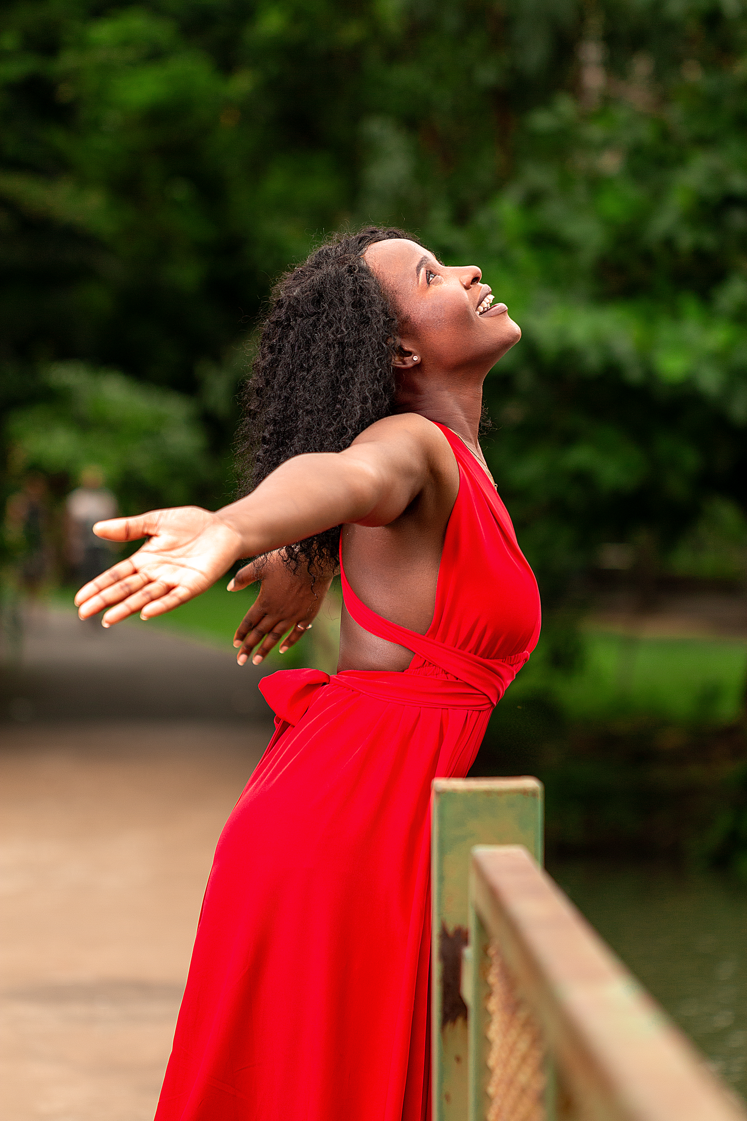 Outdoor fashion portrait in Bangkok featuring a woman in a red dress posing in a natural green location.