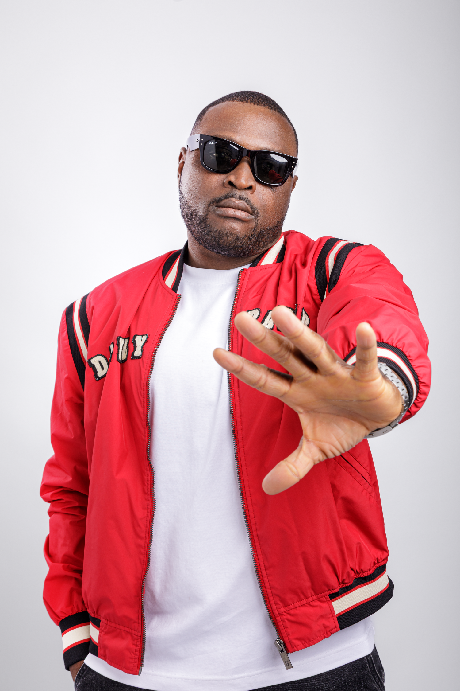 Creative studio portrait of a male artist wearing a red jacket and sunglasses with expressive posing.