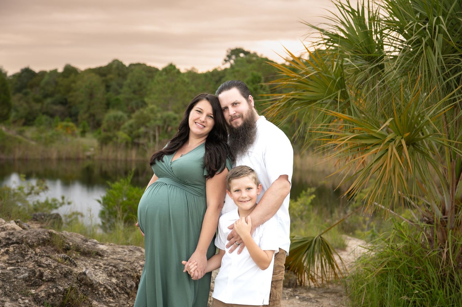 Outdoor family portraits in natural setting with palm trees and water.