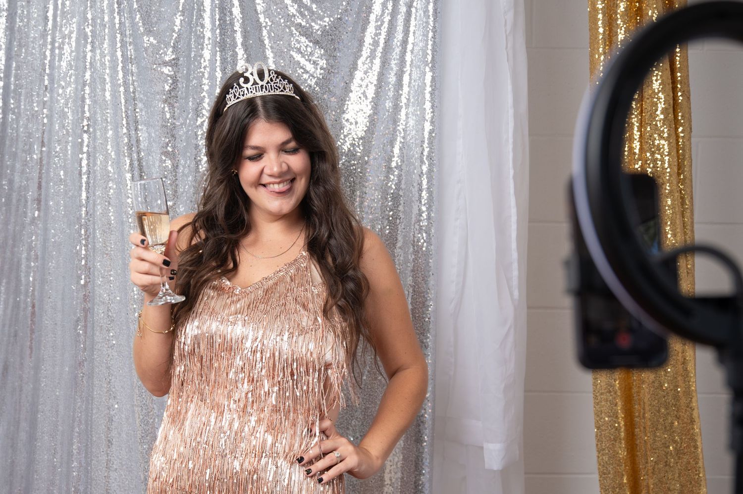 Woman in sparkly rose gold dress posing against silver sequin backdrop.