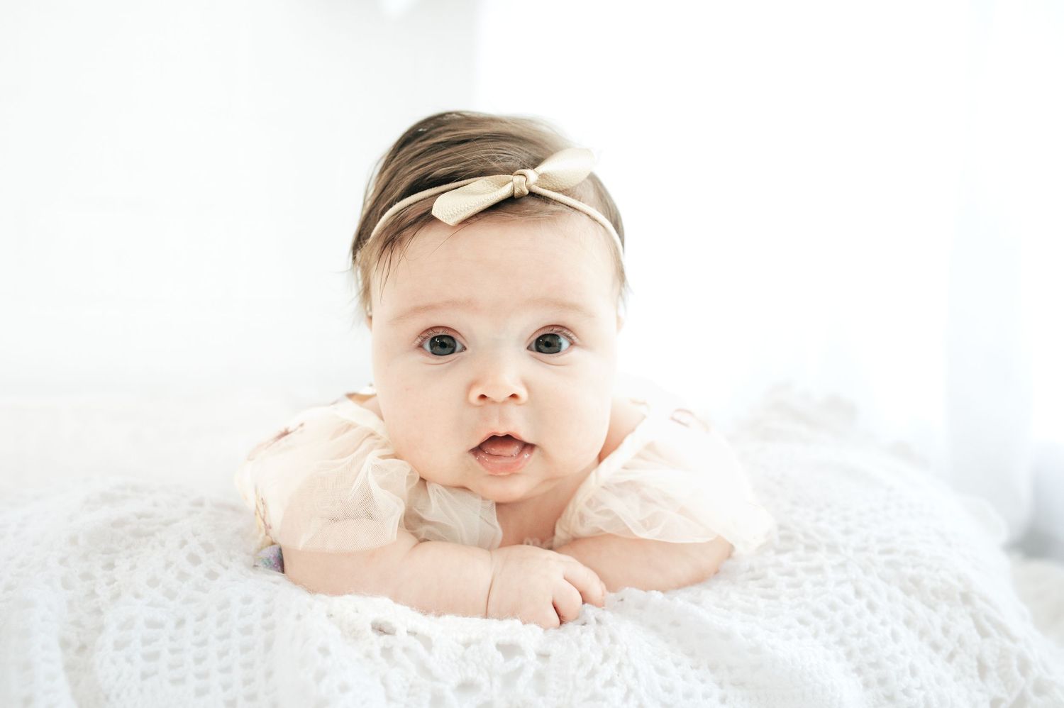 Baby in white outfit lying on textured white blanket during portrait session.