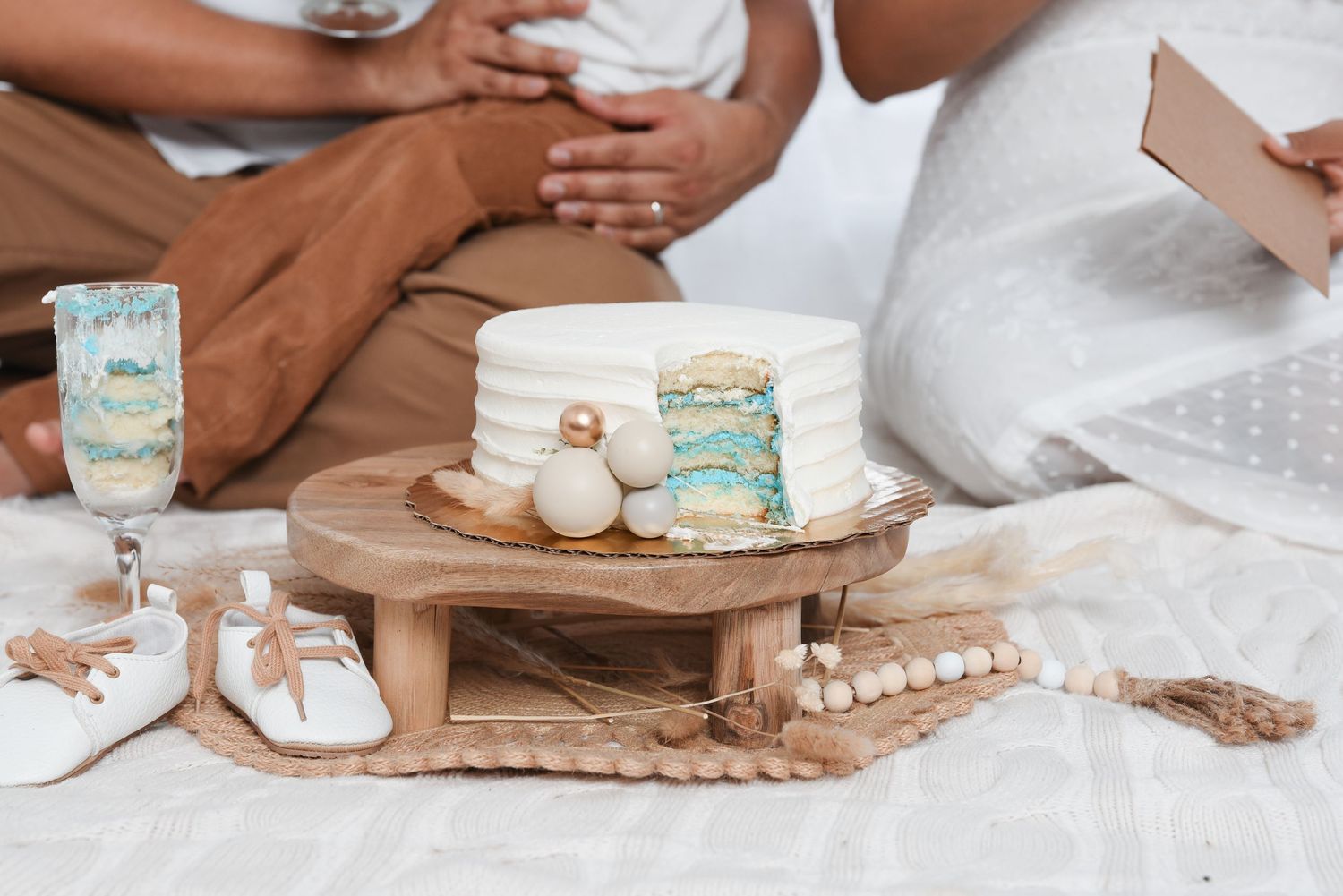 Hands placing decorative elements on a tiered white and teal wedding cake on a wooden board.