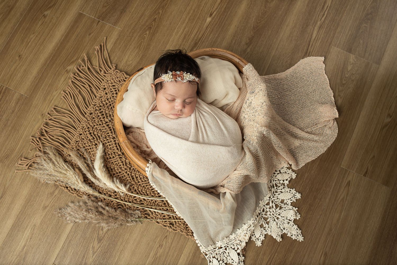 Newborn sleeping peacefully in cream wrap on textured wooden surface.