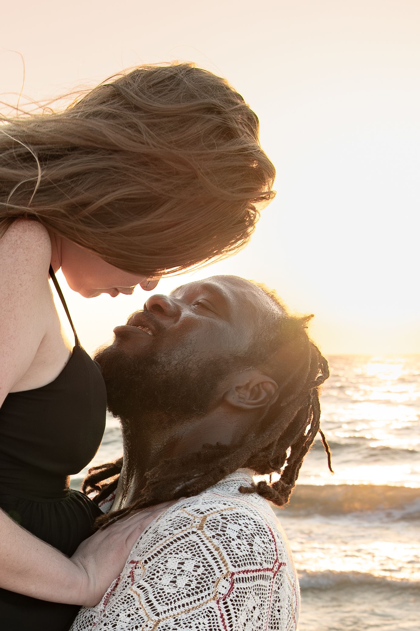 Romantic couple sharing an intimate moment at sunset on the beach with soft lighting and ocean waves in background.